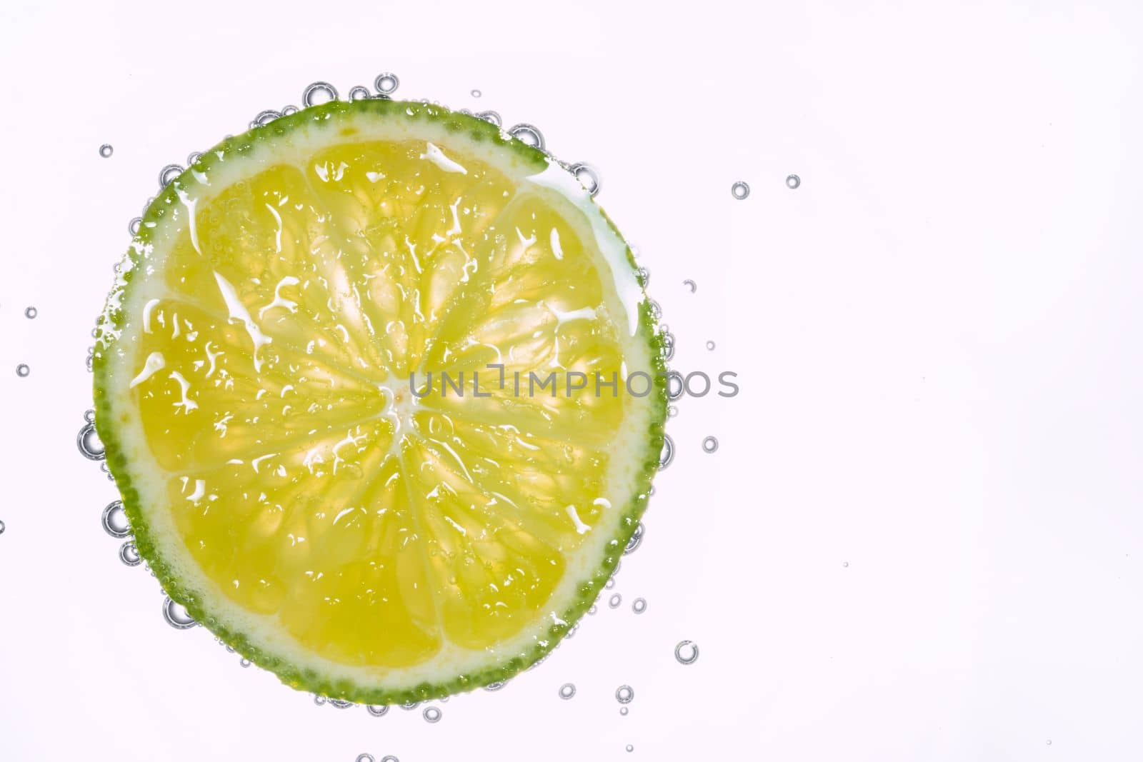 Macro photo of lime slice In water with bubbles isolated on white background. Freshness and healthy lifestyle concept. by DariaKulkova