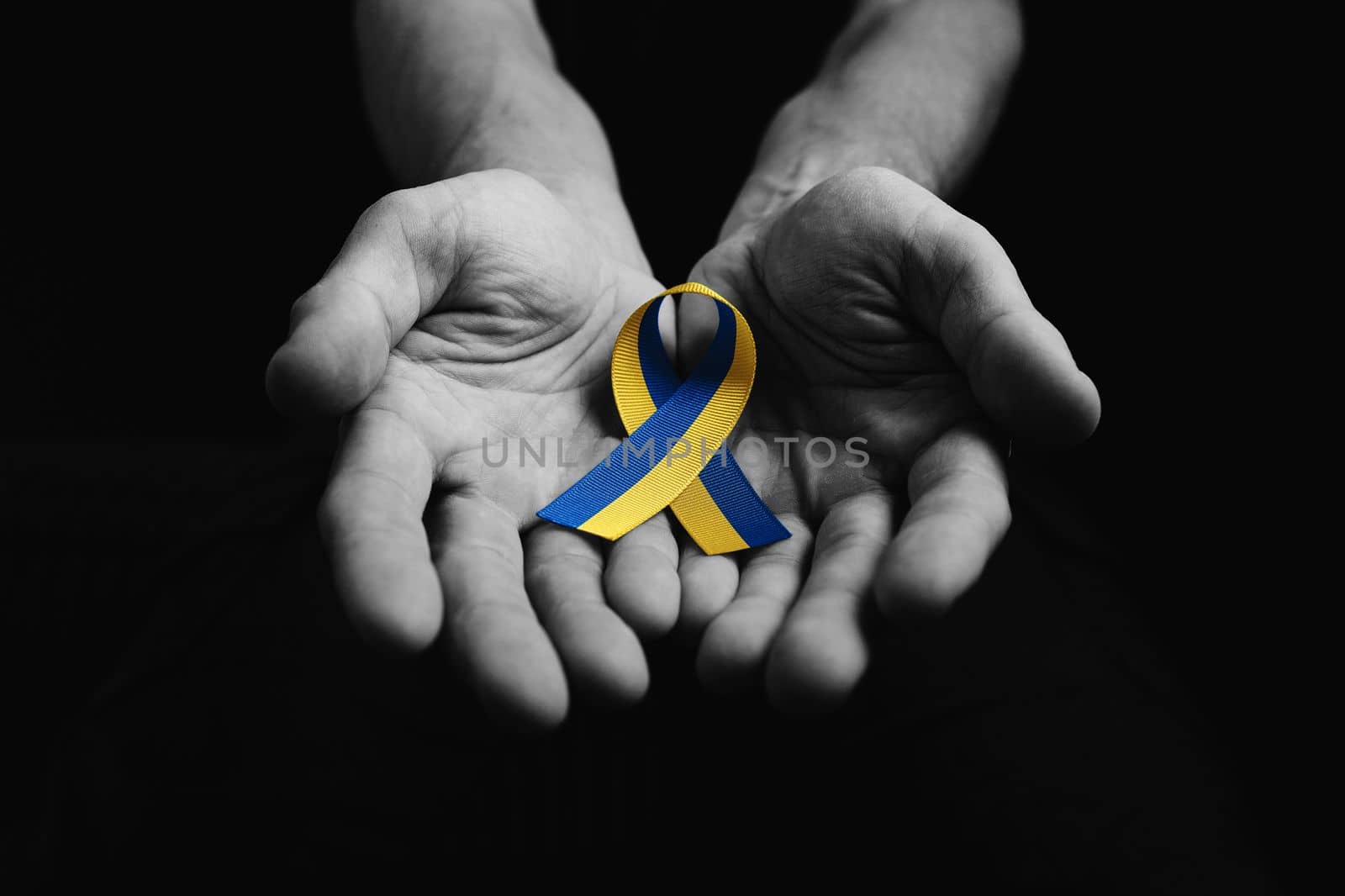 male hand holds yellow and blue ribbon on dark background. black and white color. concept needs help and support, truth will win