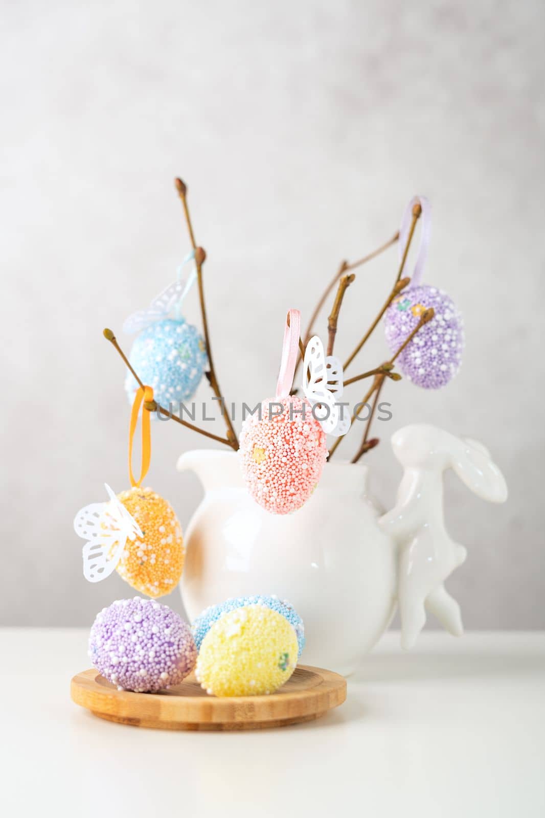 Home interior with easter decor. Vase with willow tree branches with Easter eggs and bunny on white table and background with copy space by Ostanina