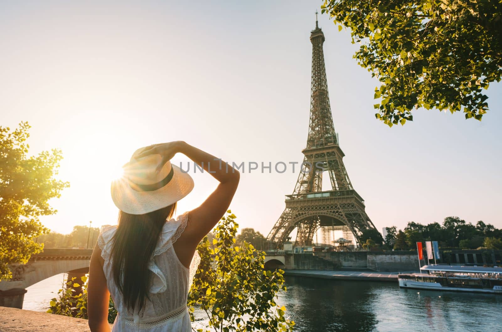Young woman tourist in sun hat and white dress standing in front of Eiffel Tower in Paris at sunset. Travel in France, tourism concept by DariaKulkova