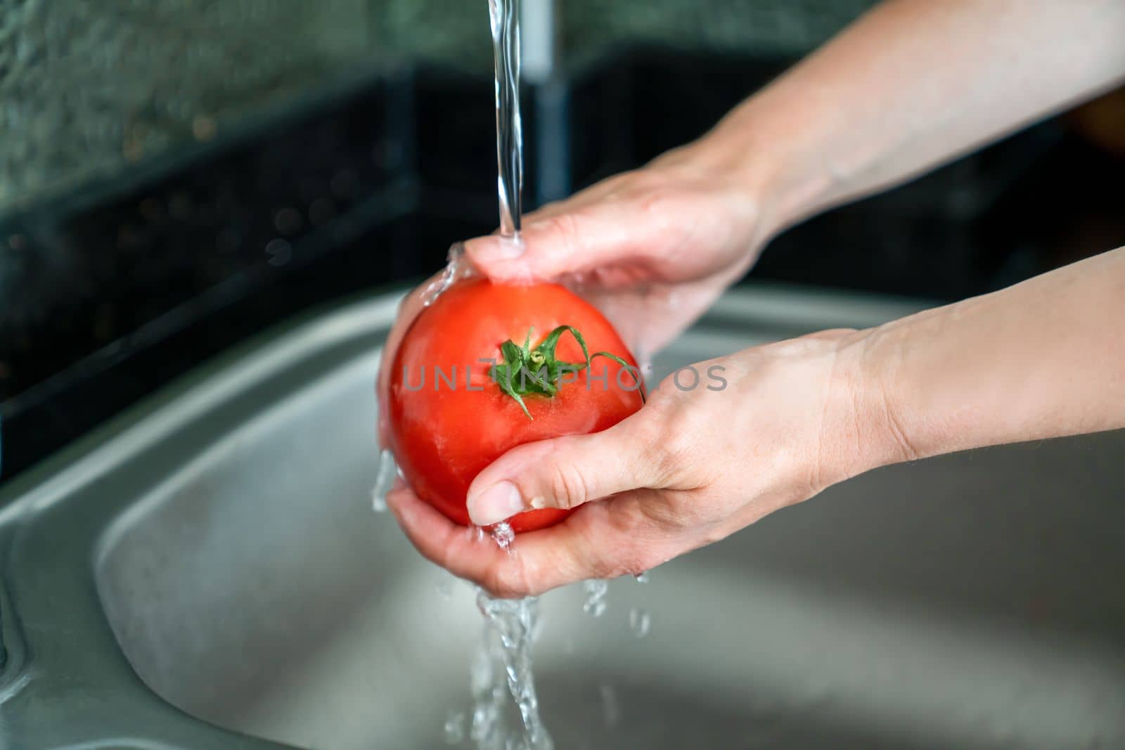 Girl washes fresh tomato over sink by Laguna781