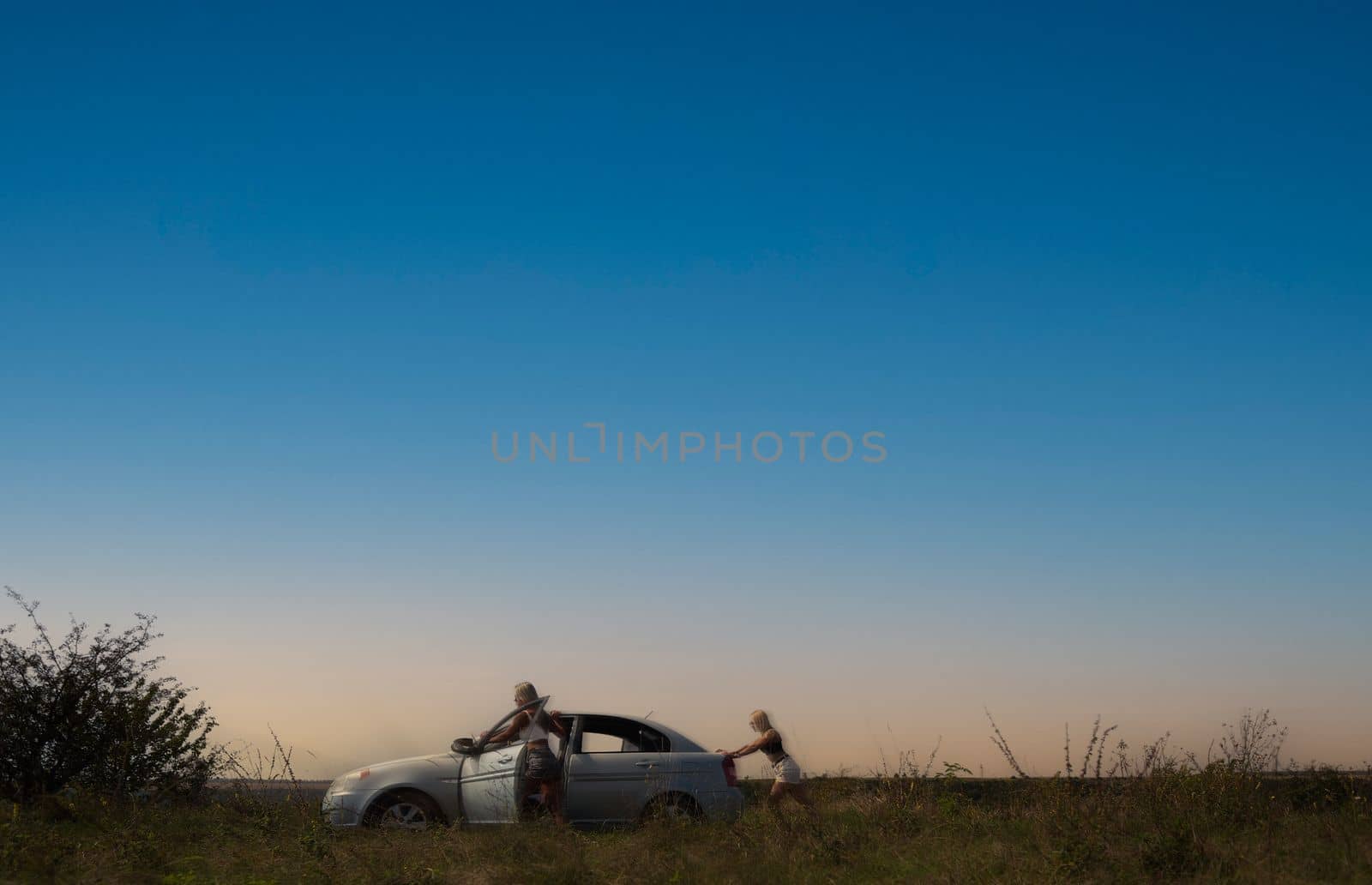 an accident on the road, a car broke down, two beautiful girl models are pushing the car for repairs. High quality photo