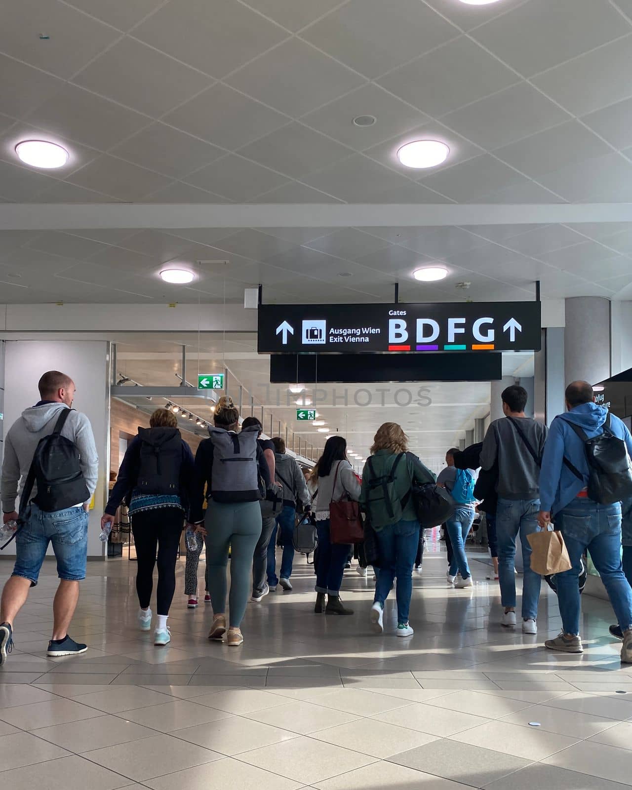 People with shoulder bags and hand luggage walking in airport terminal.