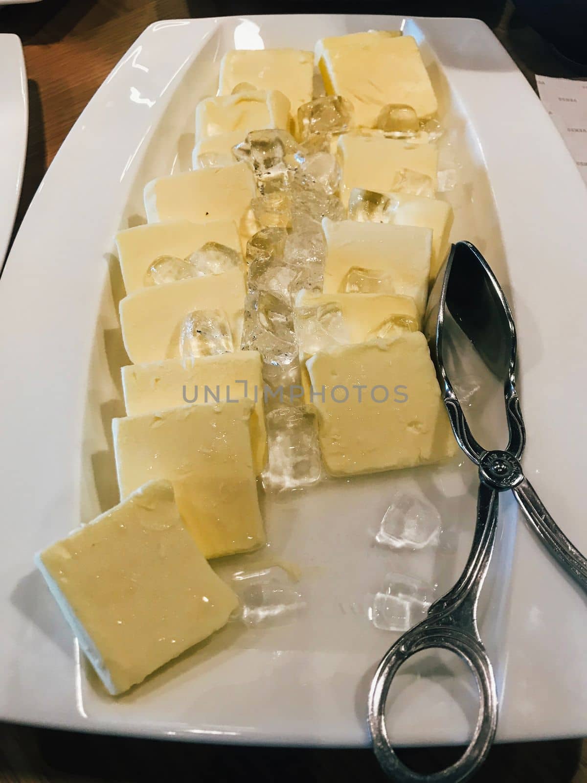 Pieces of fresh butter placing on ice in white plate. Hotel restaurant breakfast buffet.