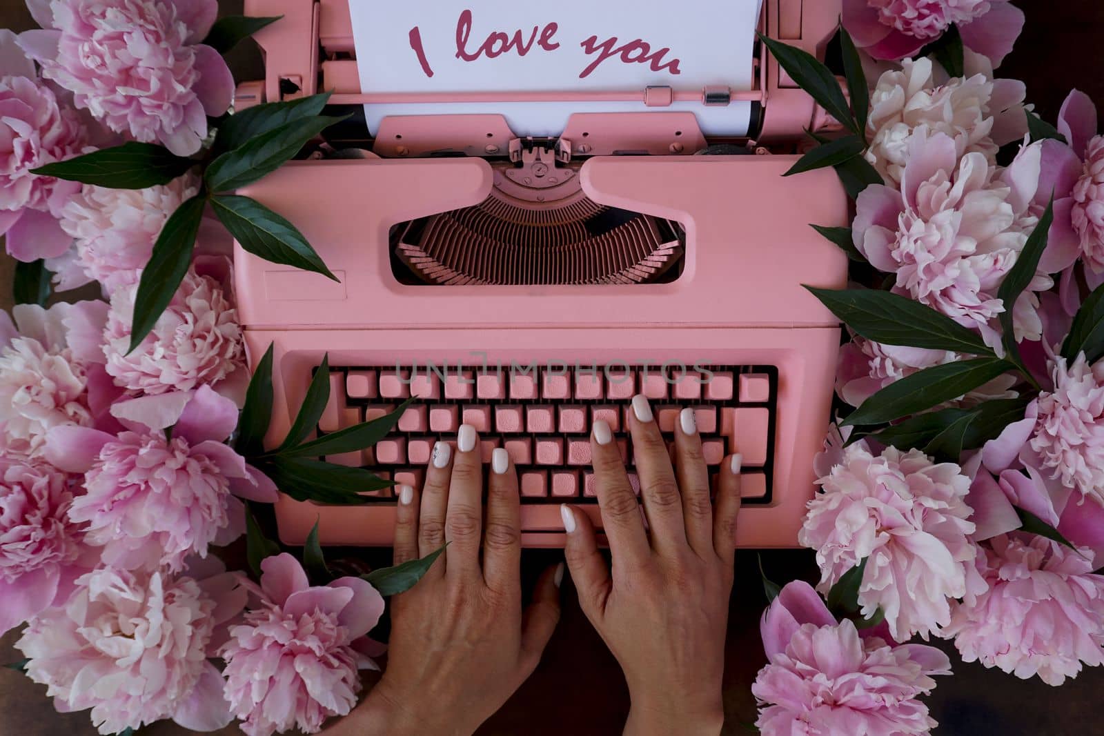 A valentine with pink peonies and a retro typewriter. Women's hands are typing the words I love you on a typewriter. Spring flatley.