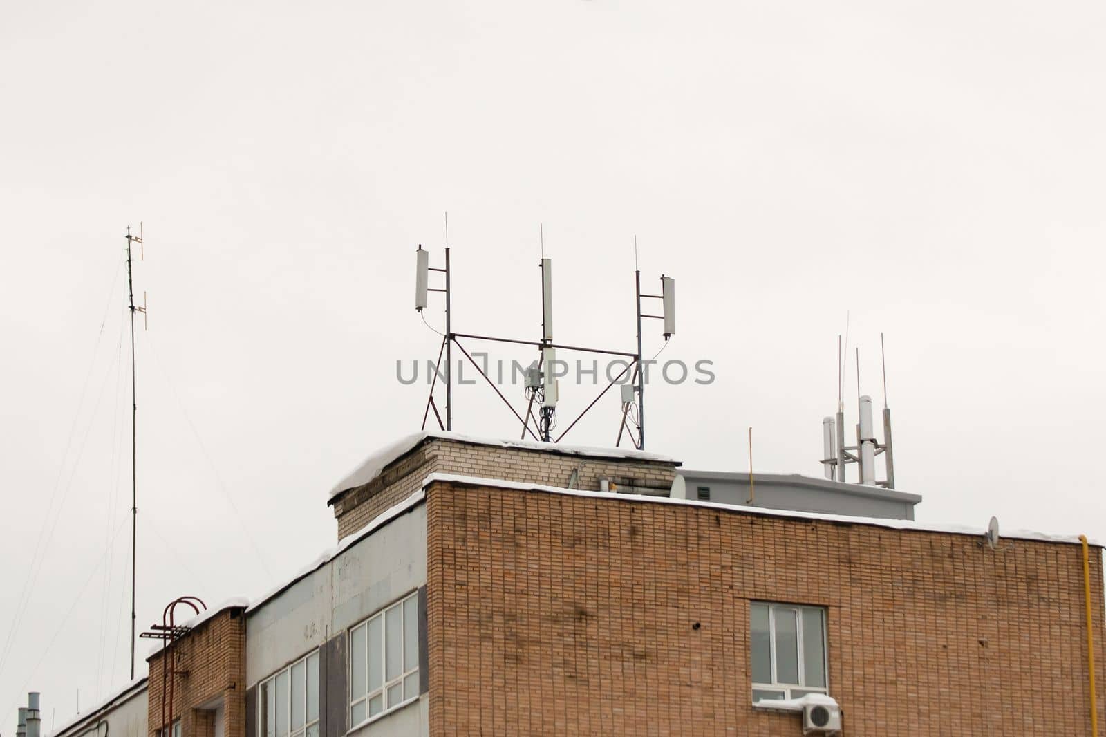 Many different cellular antennas on the roof of the house provide communication. Snow lies on the milestone, against the background of a gray sky. Cloudy, cold winter day, soft light.