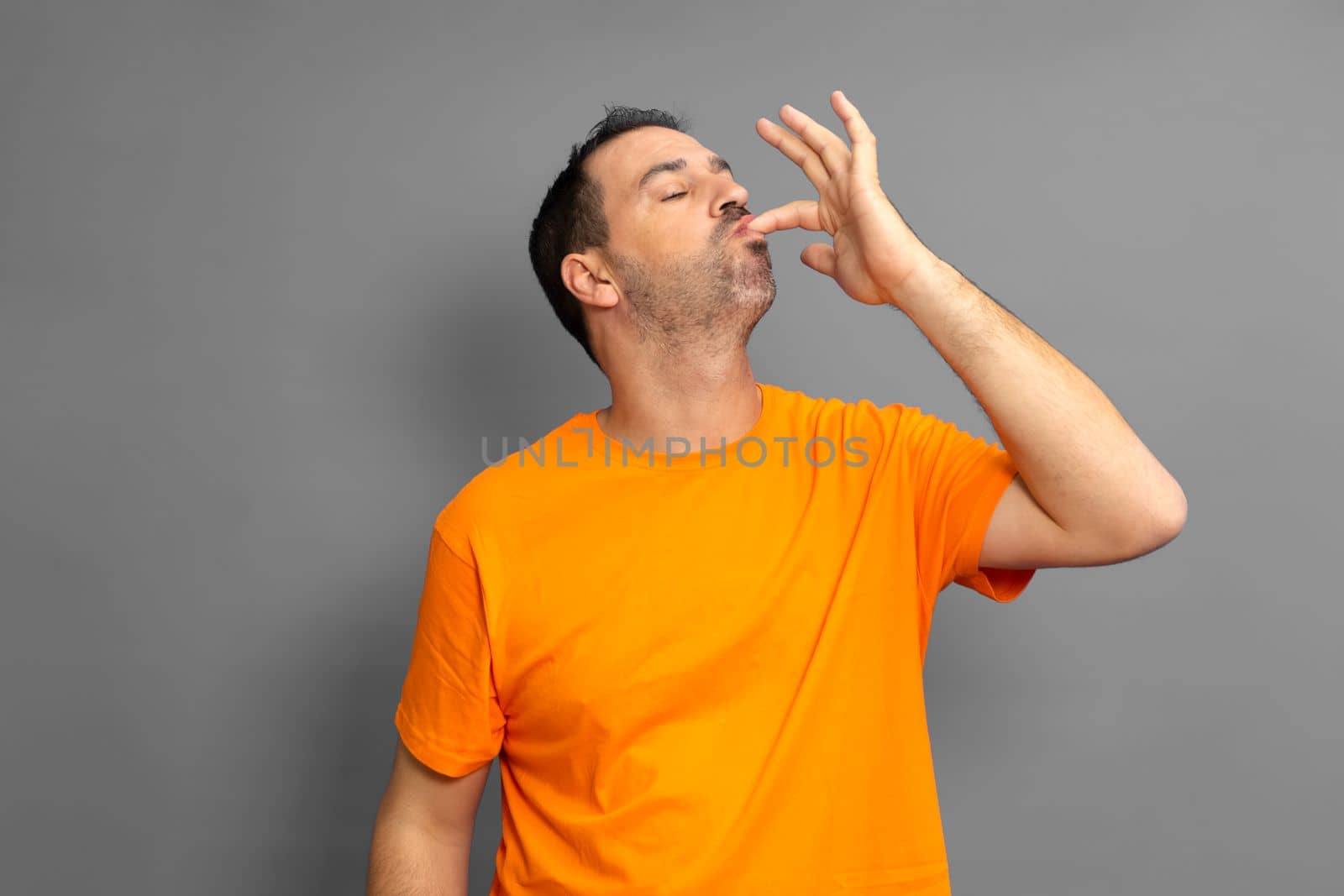 Happy man licking fingers isolated on trendy gray studio background. Beautiful male half-length portrait. Satisfied man. Human emotions, facial expression concept. Front view
