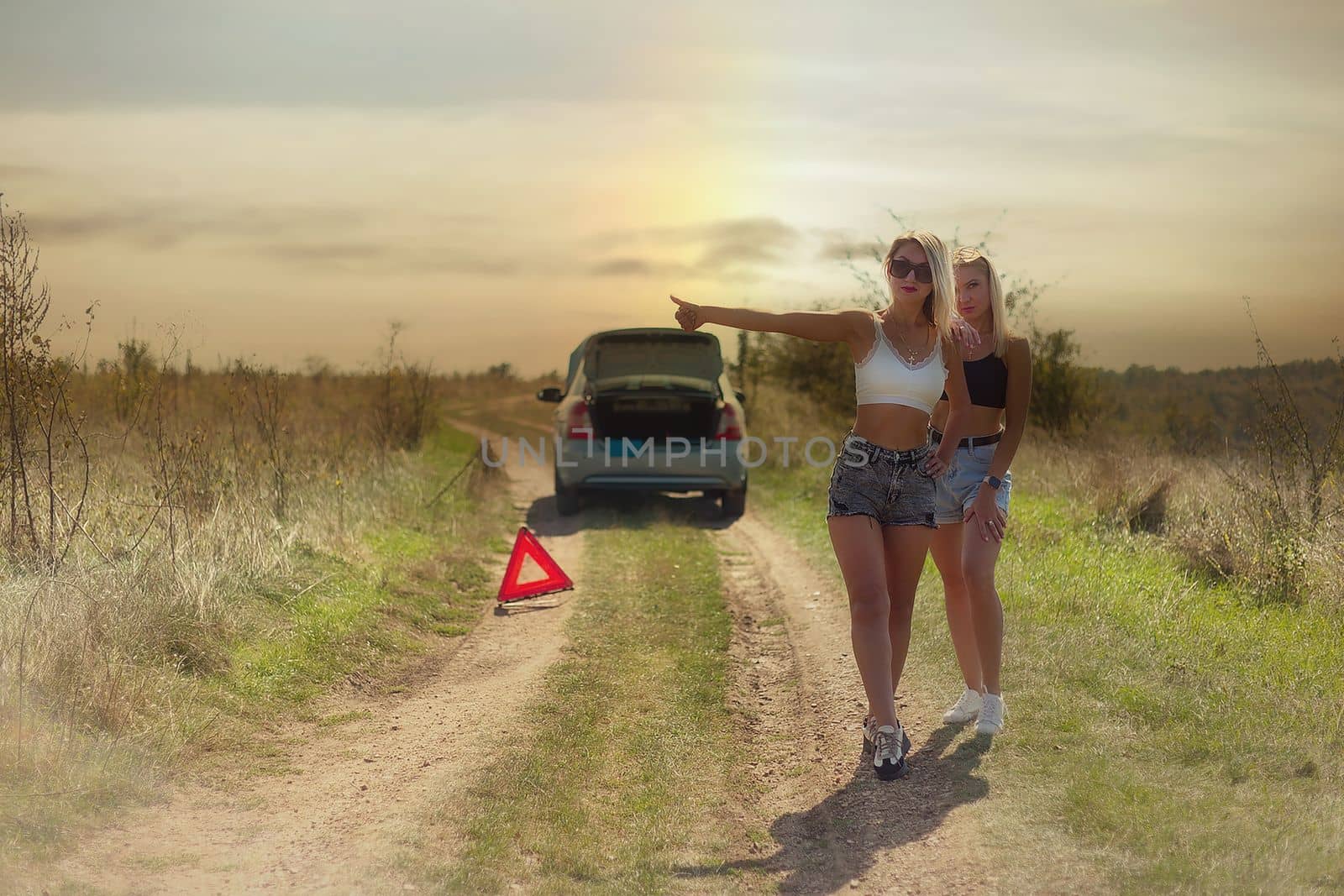 an accident on the road, a car broke down, two beautiful girl models are hitchhiking a car. Showing the thumb up. Problem with the car. Friends waiting for service. In the countryside . by marselin888