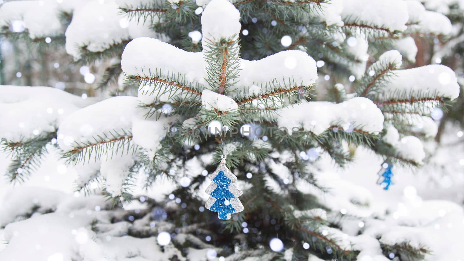Winter, festive, New Year landscape. Snow is lying on the branches of a fir tree. Snowfall. Falling snow. Christmas tree toy to lead on the branch of the Christmas tree.