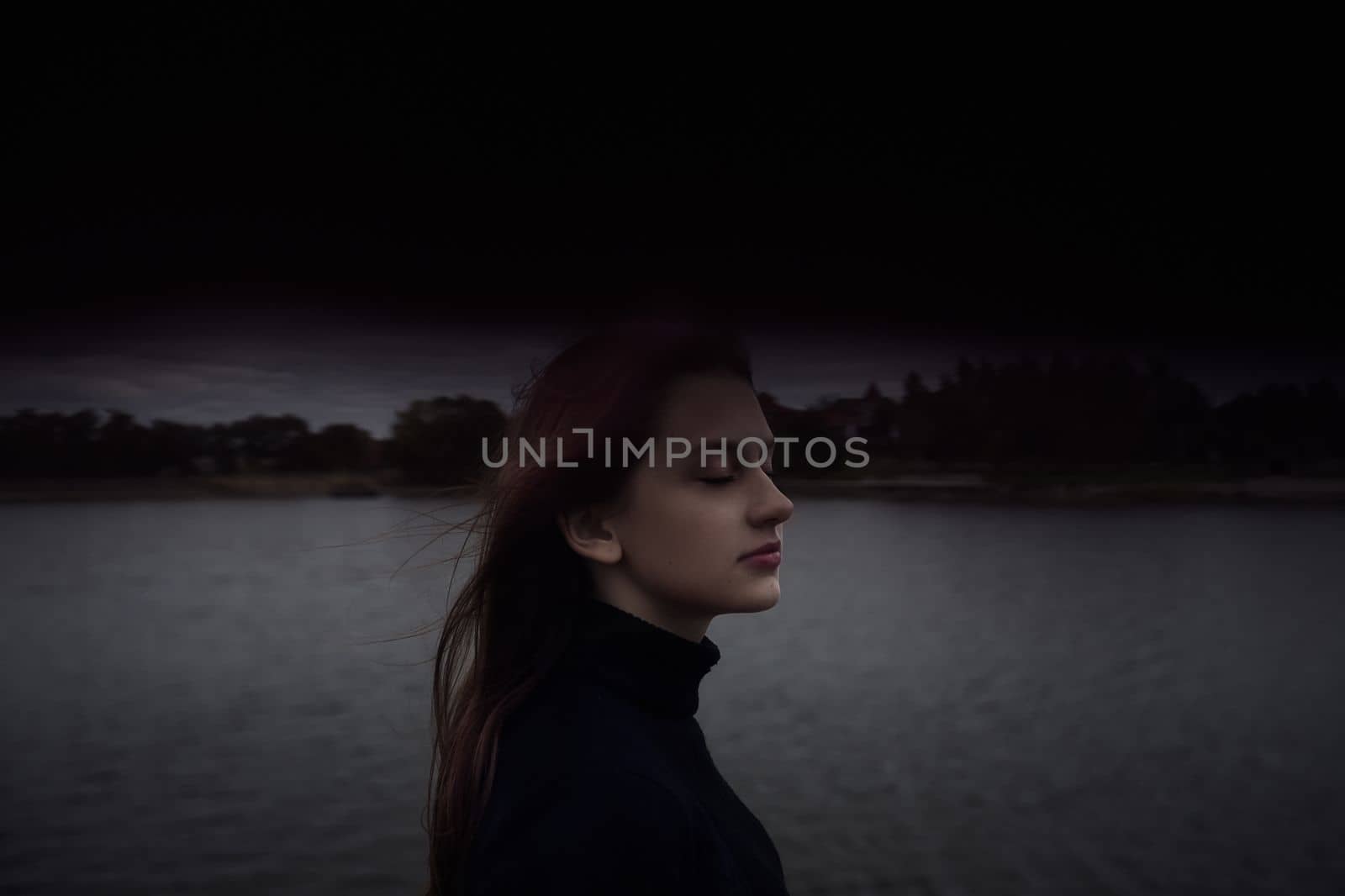 cute teenager girl closing her eyes enjoys the fresh air by the water in the evening outdoors. High quality photo