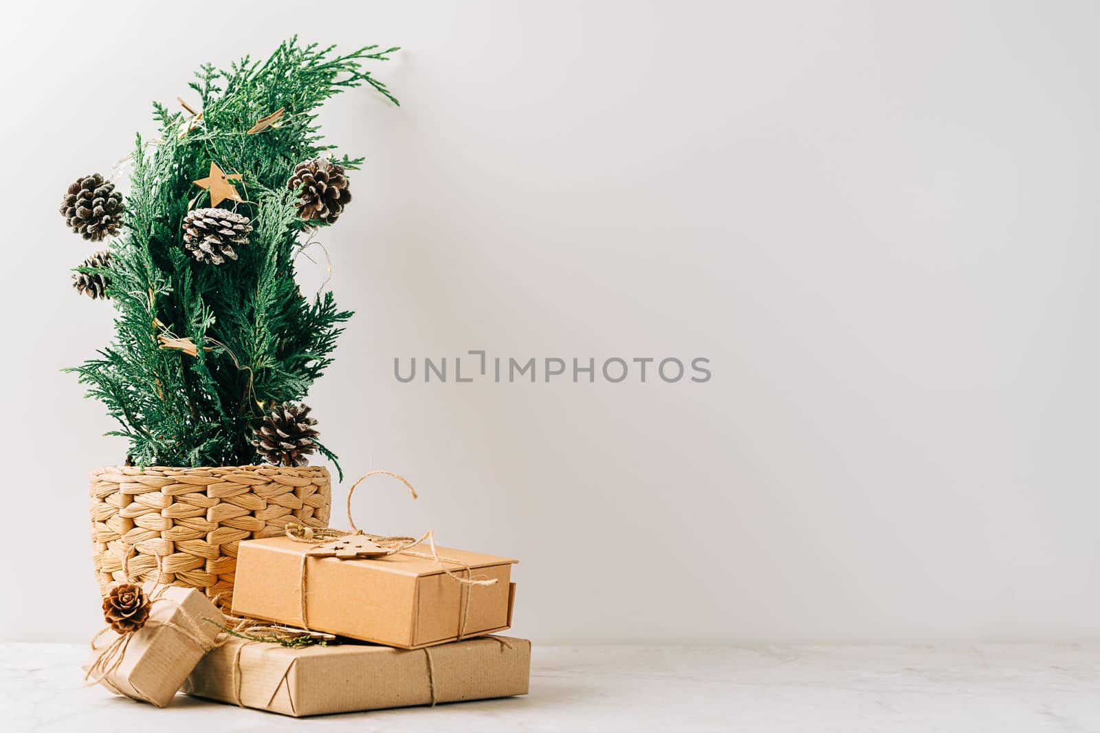 Creative natural miniature Christmas tree in pot on wooden table with gift boxes and white background. Xmas greeting card with copy space. Happy New Year