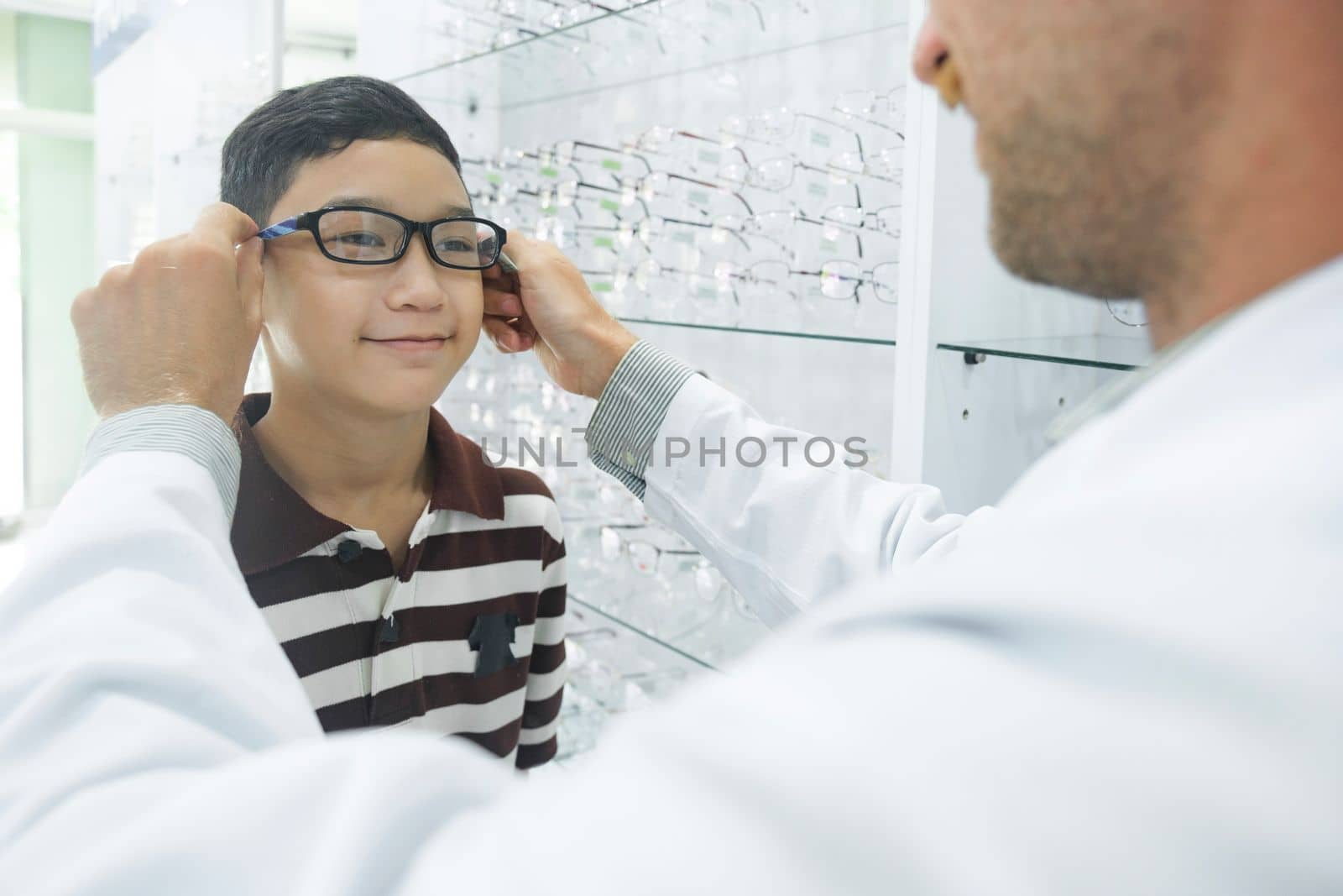 Smart young buy student in striped polo t-shirt happy trying out, testing, and choosing new eyeglasses for study with professional optician supervising at optical store.