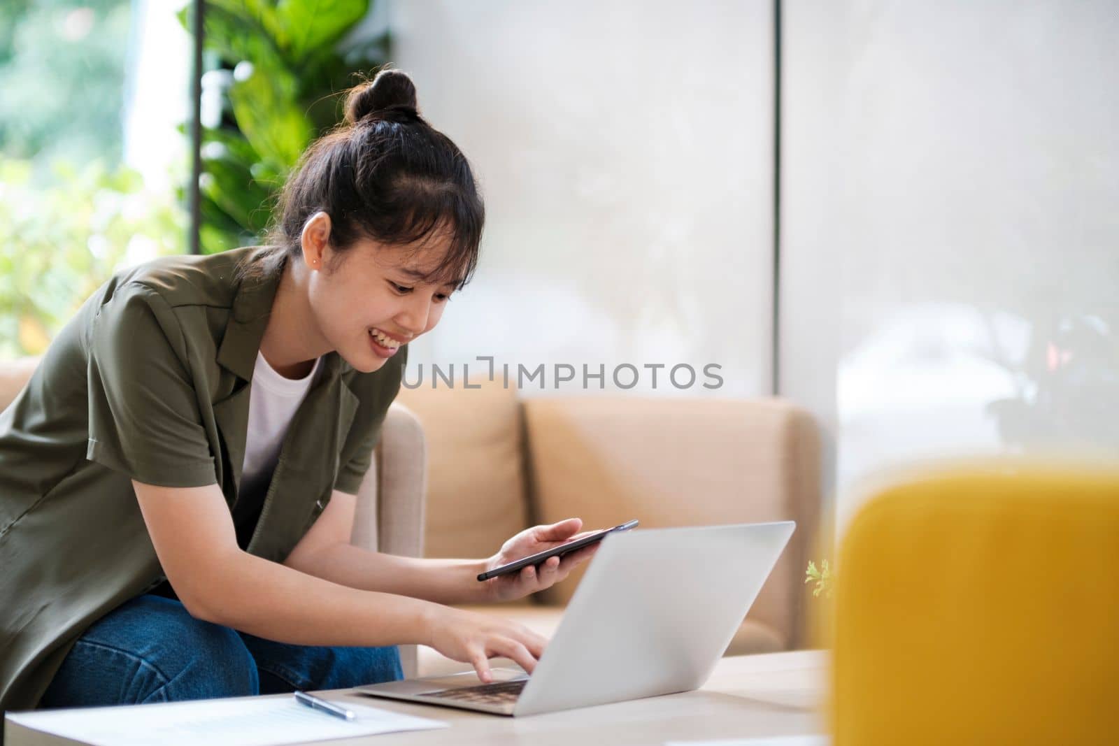 Young asian businesswoman uses a mobile phone to contact a customer, working hard at the office using laptop data graphs, planning for improvement, analyzing and strategizing for business growth. Business concept