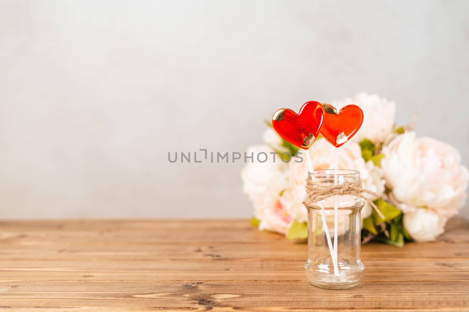 Still life Valentines day festive empty background with 2 red lollipop and pink flowers on wooden table background. Mockup with copy space for design banner.