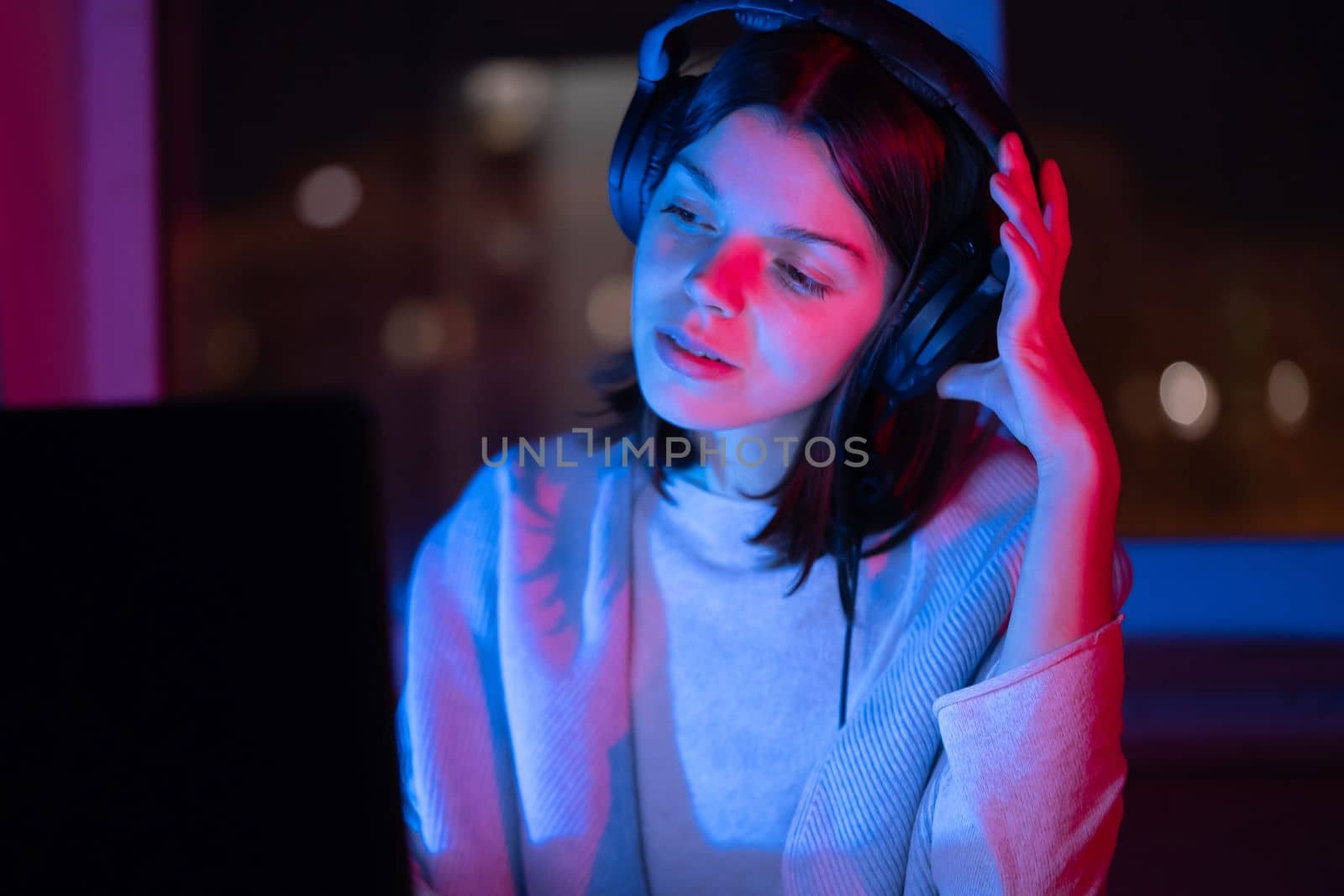 A young girl holds headphones and is listening and composing music, a woman sits with a laptop by the window in her room, works and enjoys the sound.