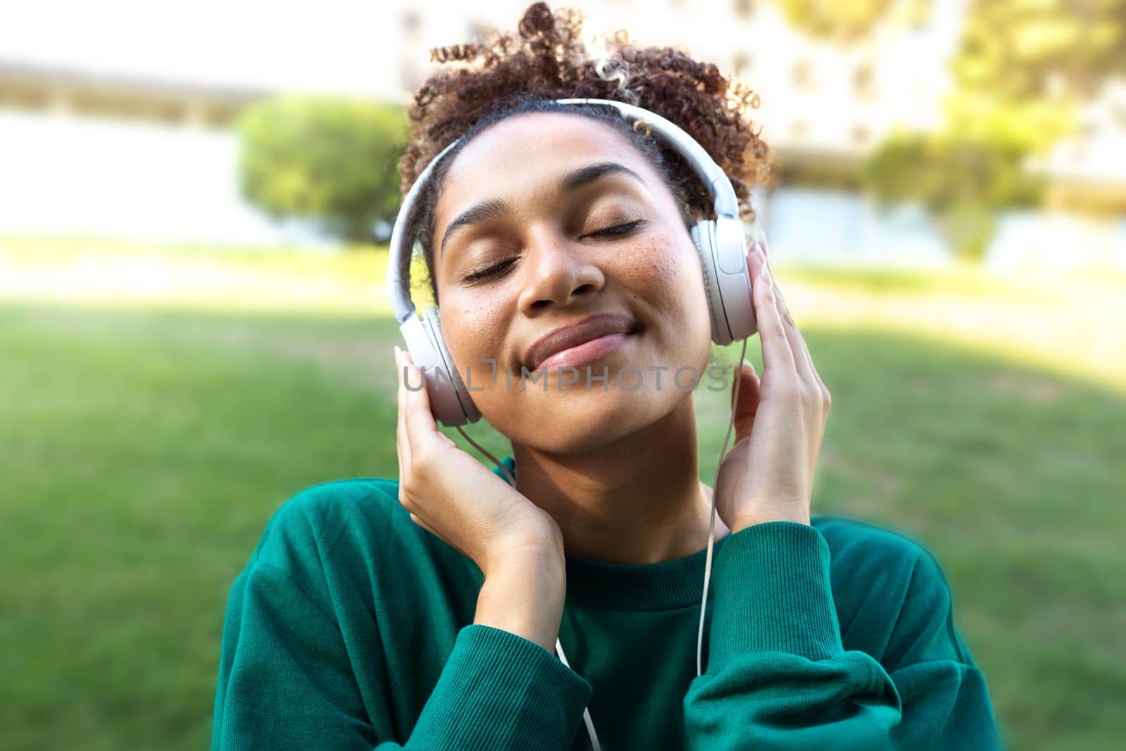 African American young woman with closed eyes relaxing outdoors listening to music using headphones. Lifestyle concept.