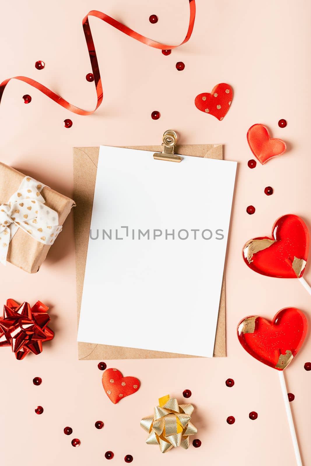 Flat lay of paper envelope with blank mockup greeting paper card. Pink table background with Valentine day gift, letter, heart shape, confetti, lollipops and decoration. Top view, mock up invitations. by Ostanina