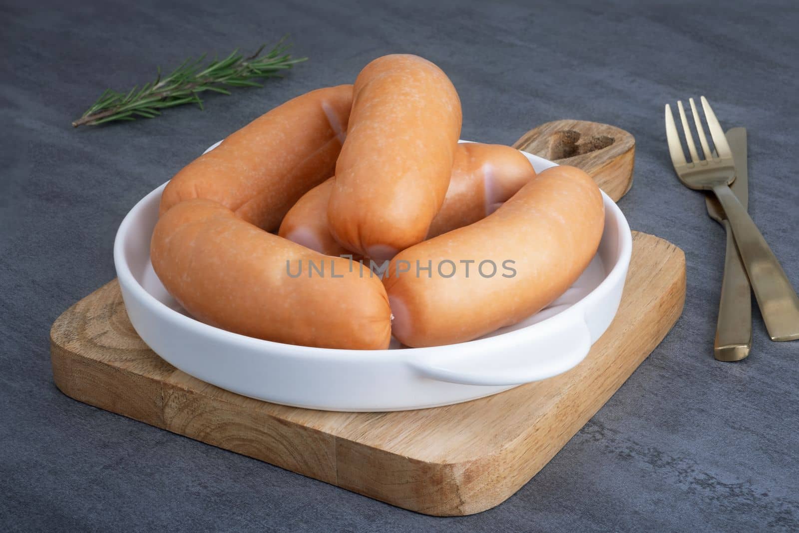 Several sausages lie in a white ceramic dish on a wooden cutting board. Selective focus.
