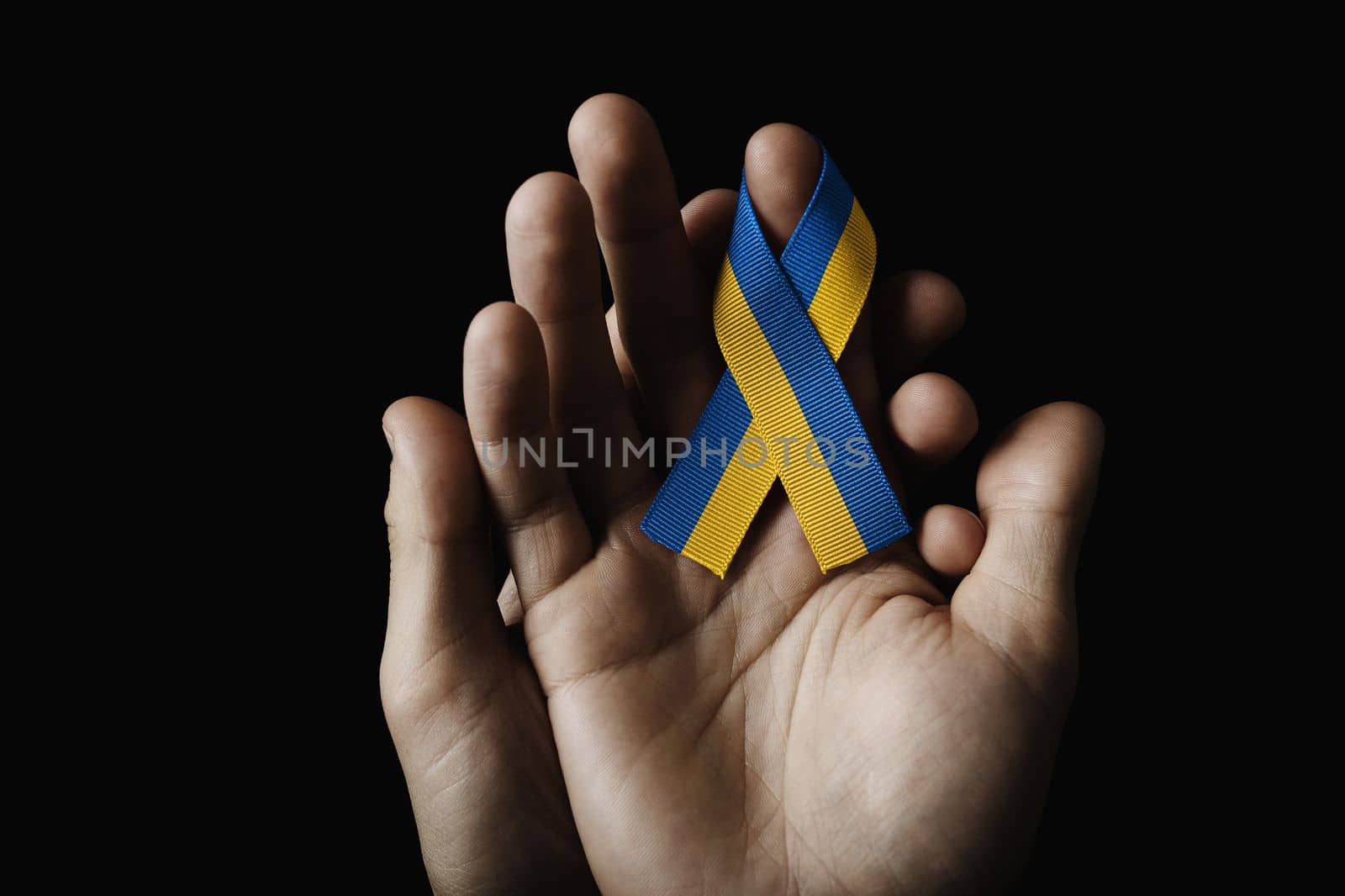 hand in hand holding a blue yellow ribbon on a dark background. concept needs help and support, truth will win