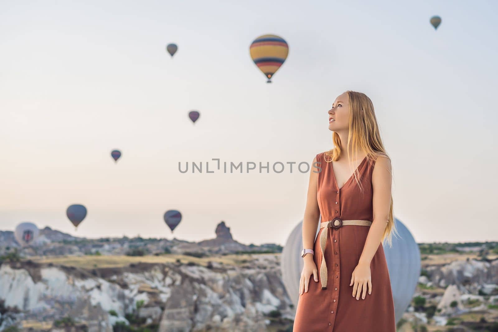 Tourist woman looking at hot air balloons in Cappadocia, Turkey. Happy Travel in Turkey concept. Woman on a mountain top enjoying wonderful view.