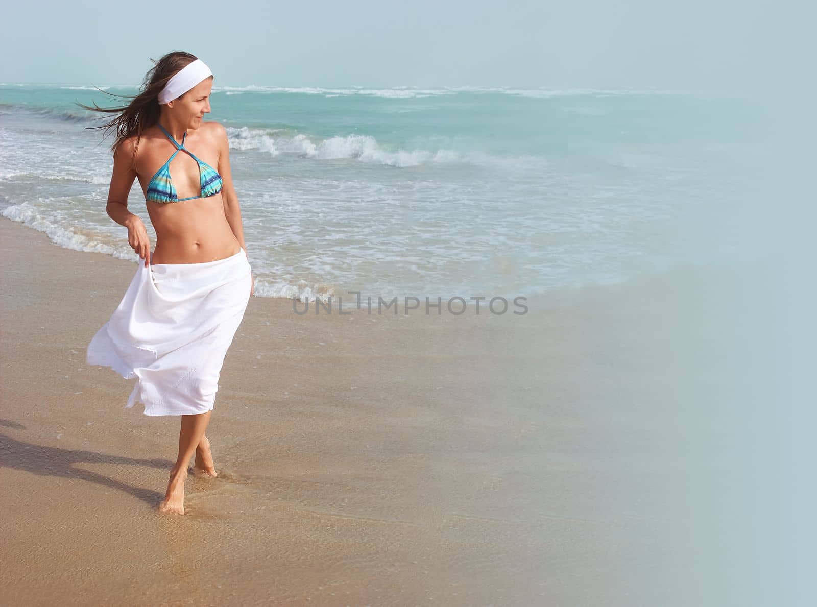 Beautiful happy girl walks barefoot, on sandy beach, along ocean, wind is blowing her hair and white skirt. Concept of travel, relaxation, happiness and freedom, copy space