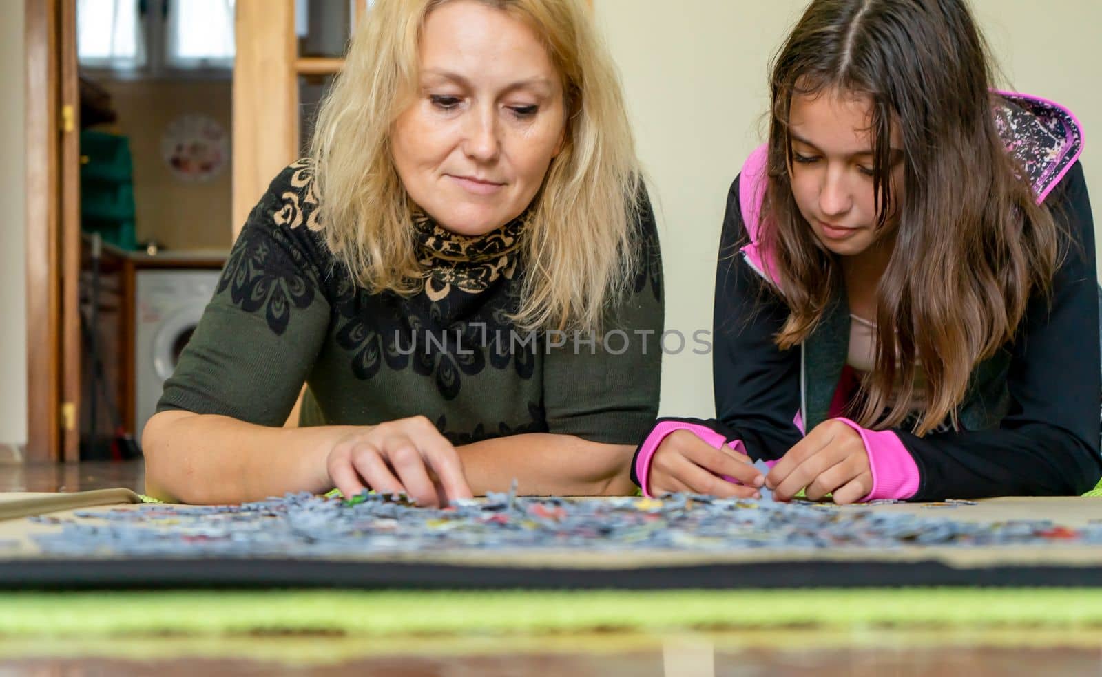 Mother and daughter lying on the floor doing a puzzle together while having a nice time on a girls night out.