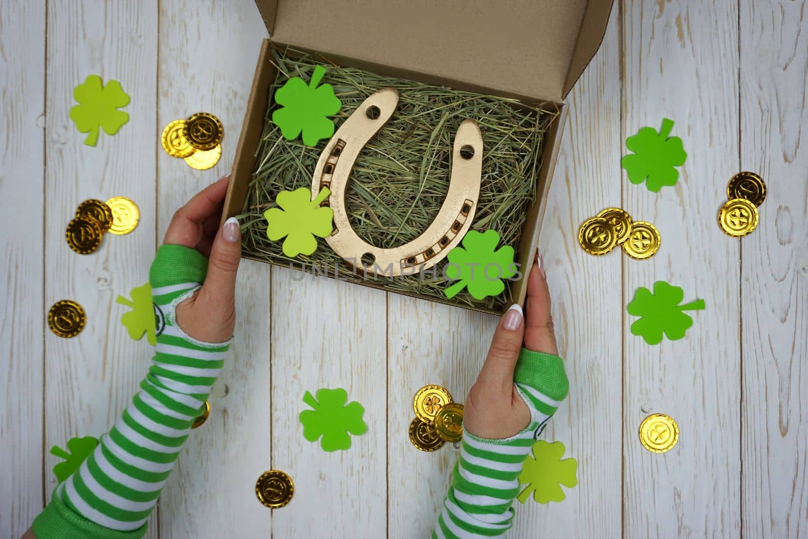 Women's hands hold a box with a gift for St. Patrick's Day. Horseshoe in a craft box filled with fresh hay. Background.