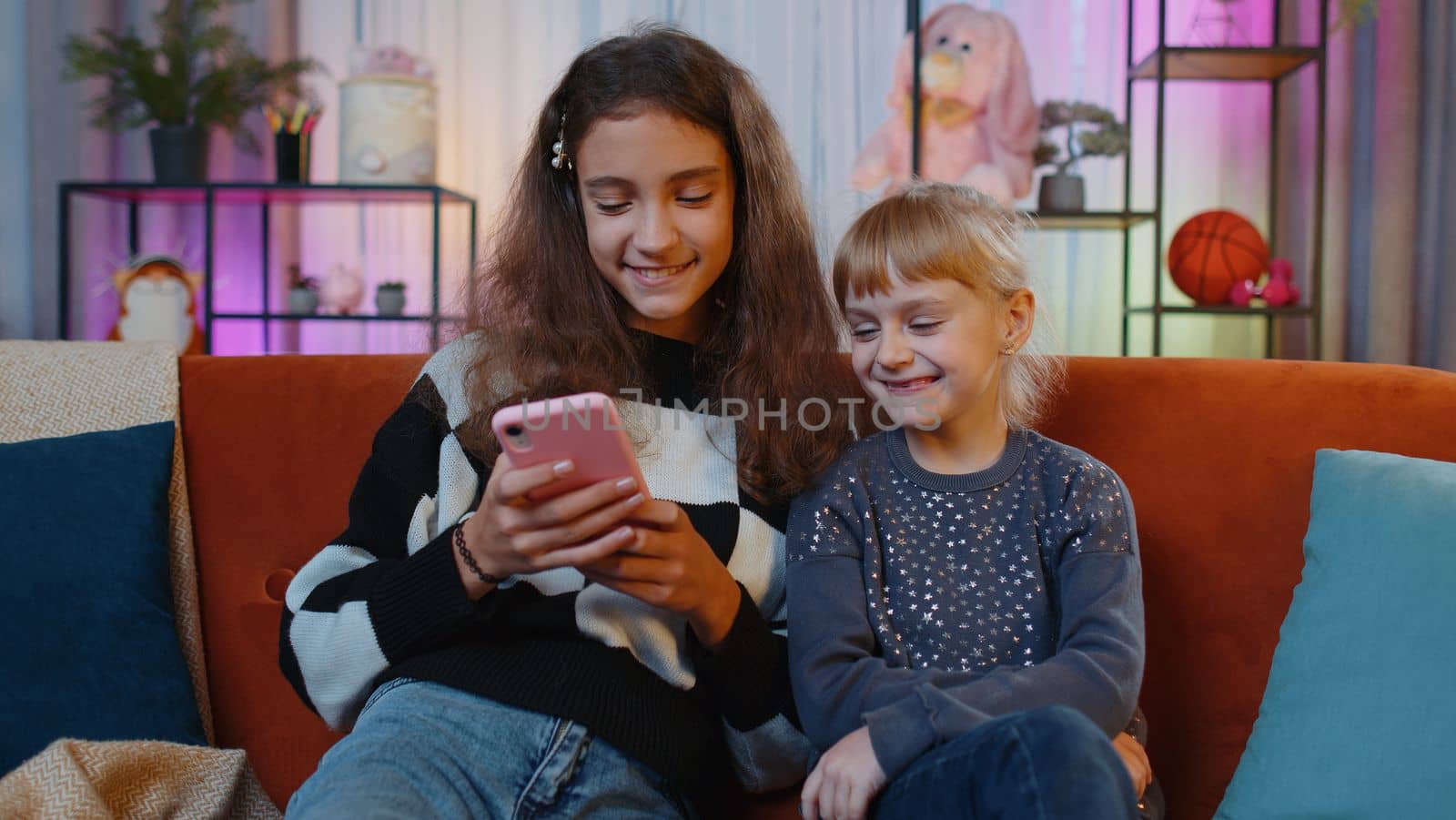 Teen sisters kids celebrate success win scream rejoices while doing online shopping on smartphone. Happy siblings children or best friends spend leisure time on social media app at home play room