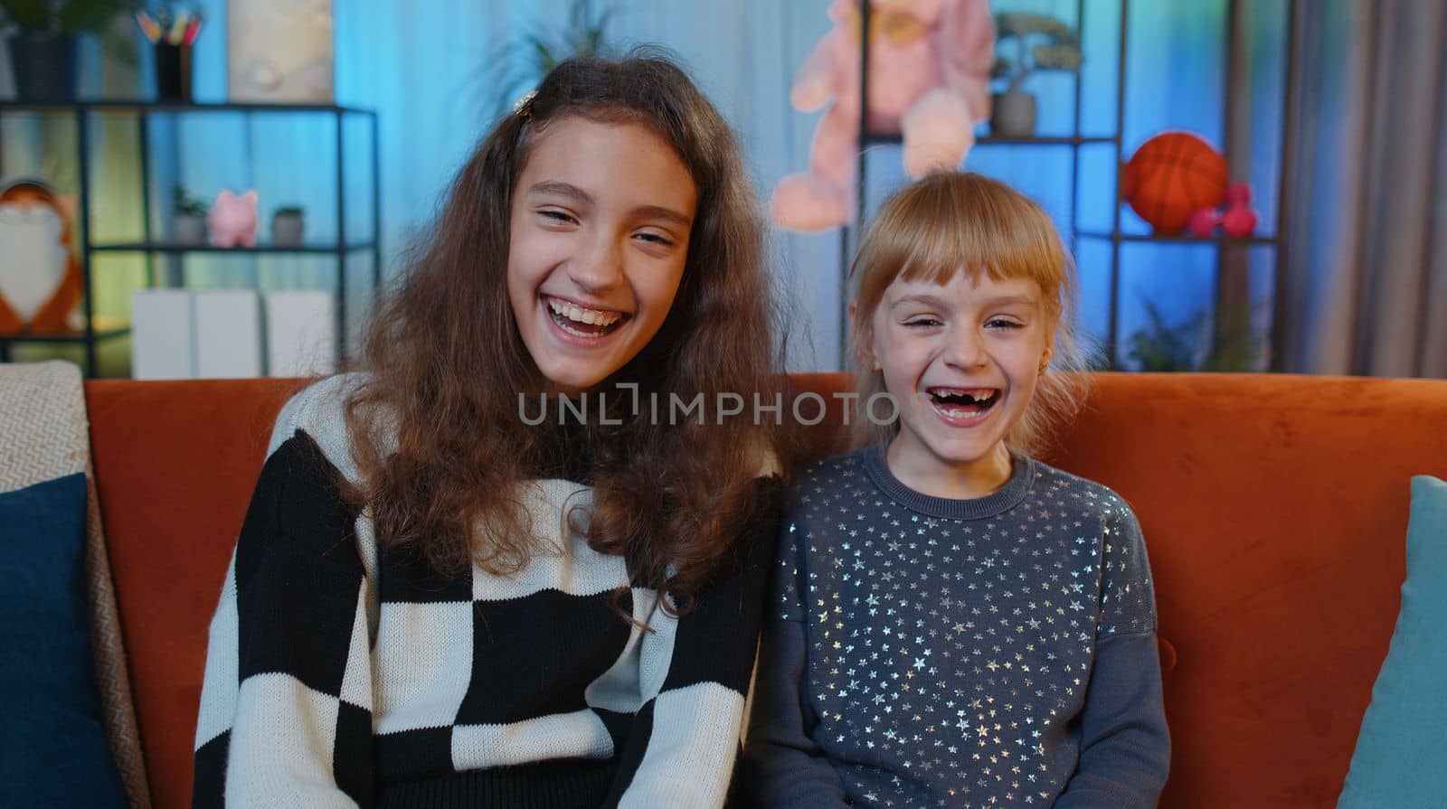 Happy teenage child and little sister kid laughing out loud after hearing ridiculous anecdote, funny joke, feeling carefree amused, positive. Female siblings children or best friends at home play room