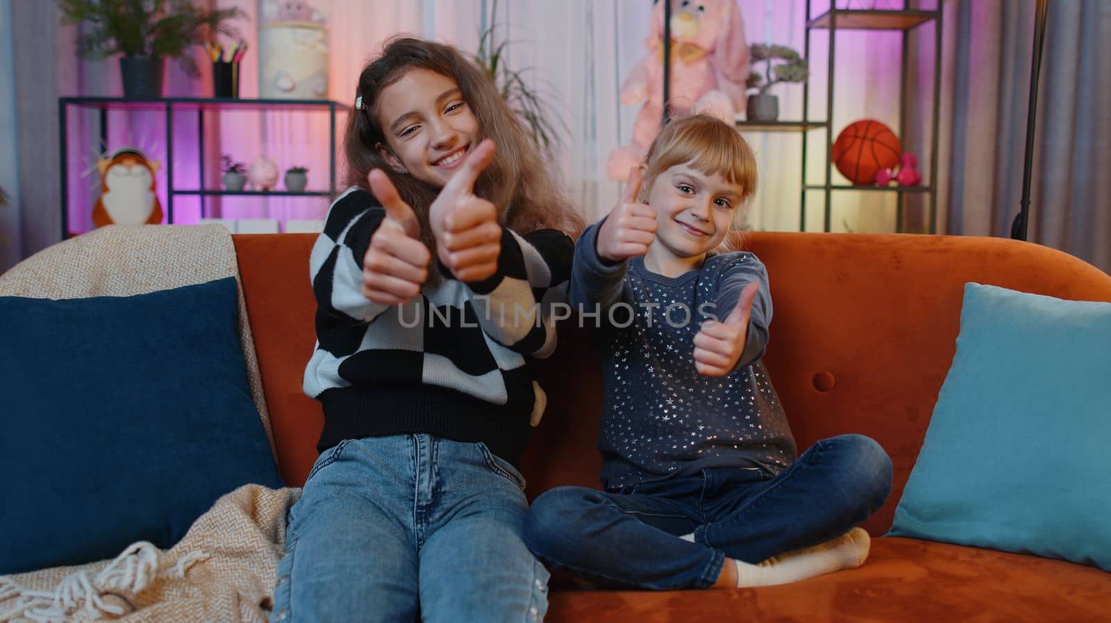 Like. Happy teenage child and little sister kid looking approvingly at camera showing thumbs up, like sign positive something good, positive feedback. Siblings children or friends at home play room