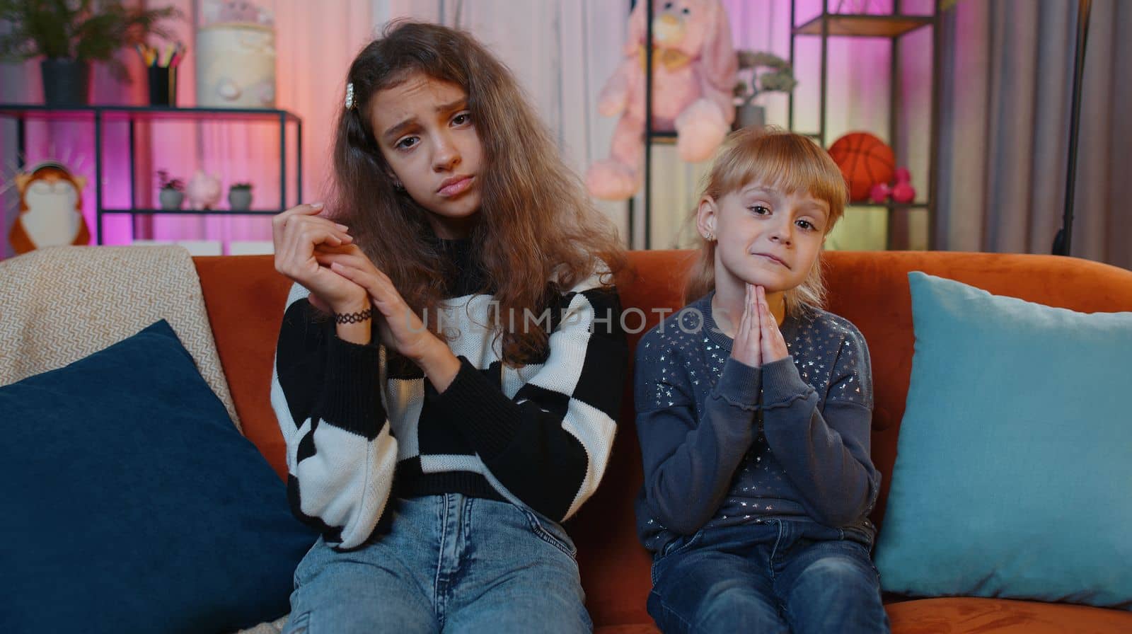 Child little sister kid girls praying sincerely with folded arms, looking upward and making wish, asking with hopeful imploring expression, begging apology. Siblings children or best friends at home