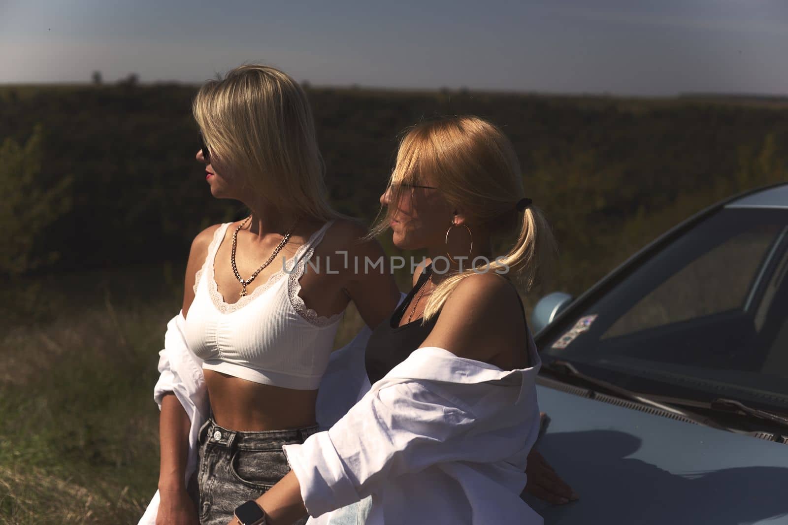 skinny girls are relaxing near a broken car away from the bustle of the city, best friends are free and enjoy the journey. High quality photo