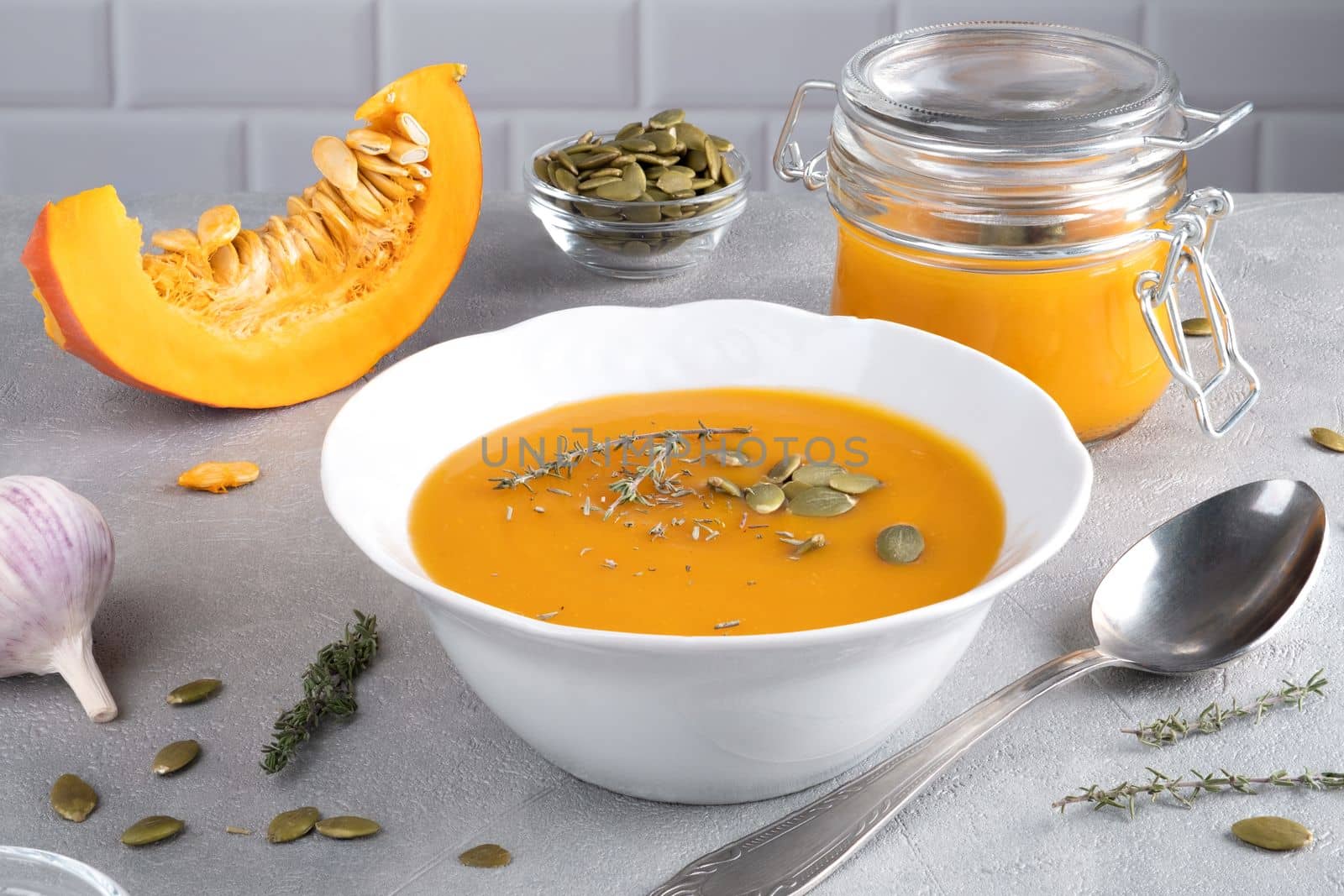 Pumpkin puree soup with pumpkin seeds and thyme in a white plate and glass jar. Healthy diet. Selective focus.