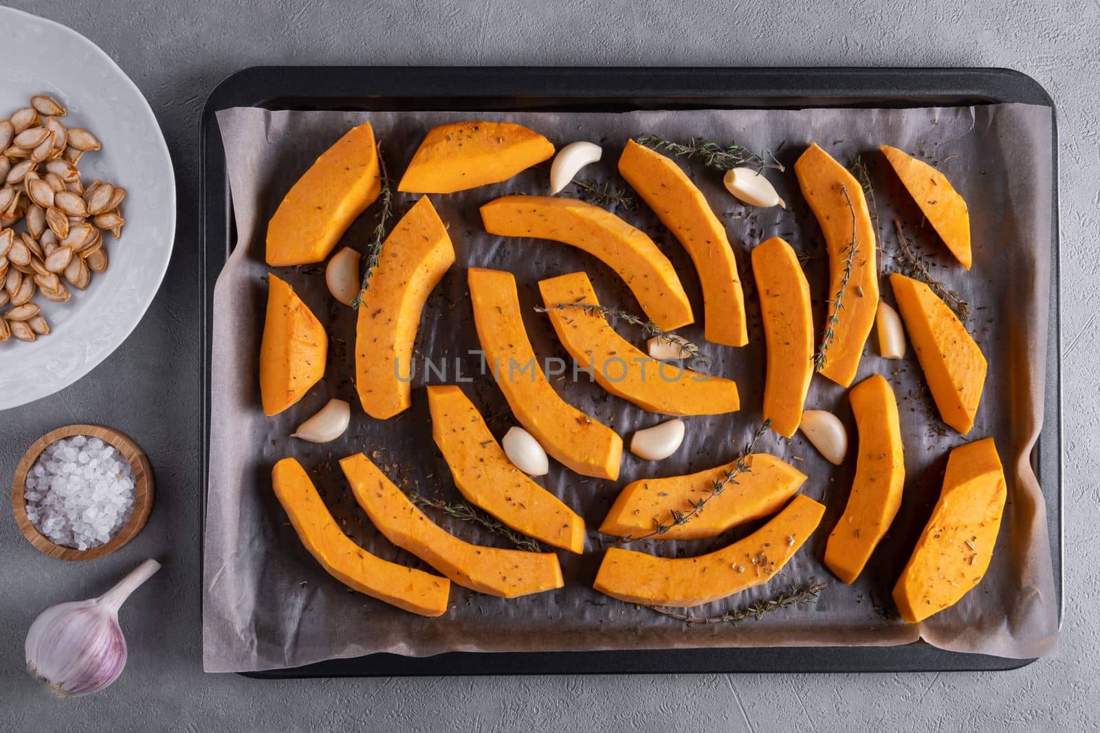 Pieces of ripe pumpkin prepared for baking in the oven. Pumpkin on a baking sheet with olive oil, garlic and dry thyme on the kitchen table. Healthy food. View from above. Selective focus.