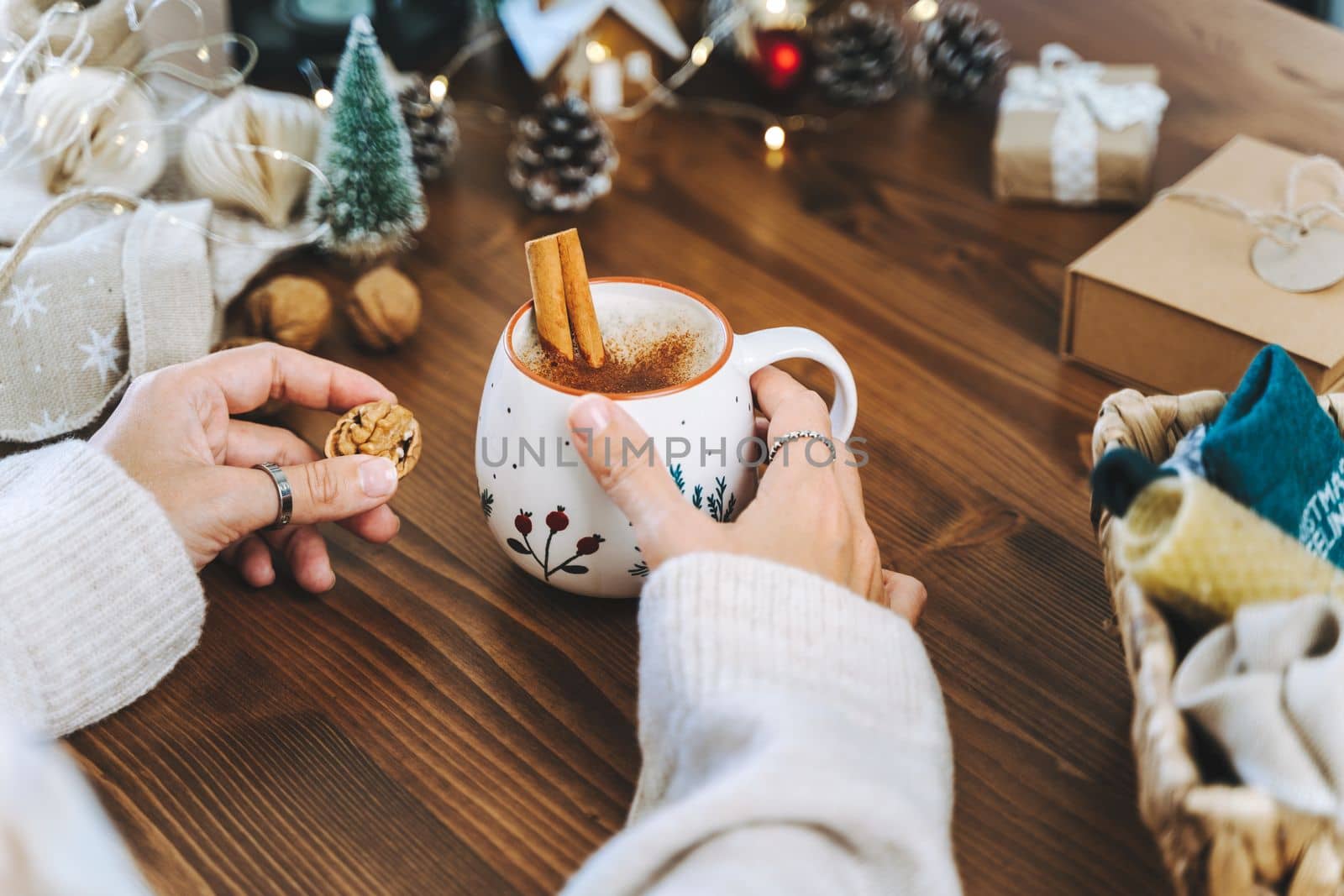 Christmas mug of coffee with cinnamon in woman hands. Wrapping Christmas eco gift box, close up. Preparing presents on wooden table with natural decor elements and items Christmas packing Concept.