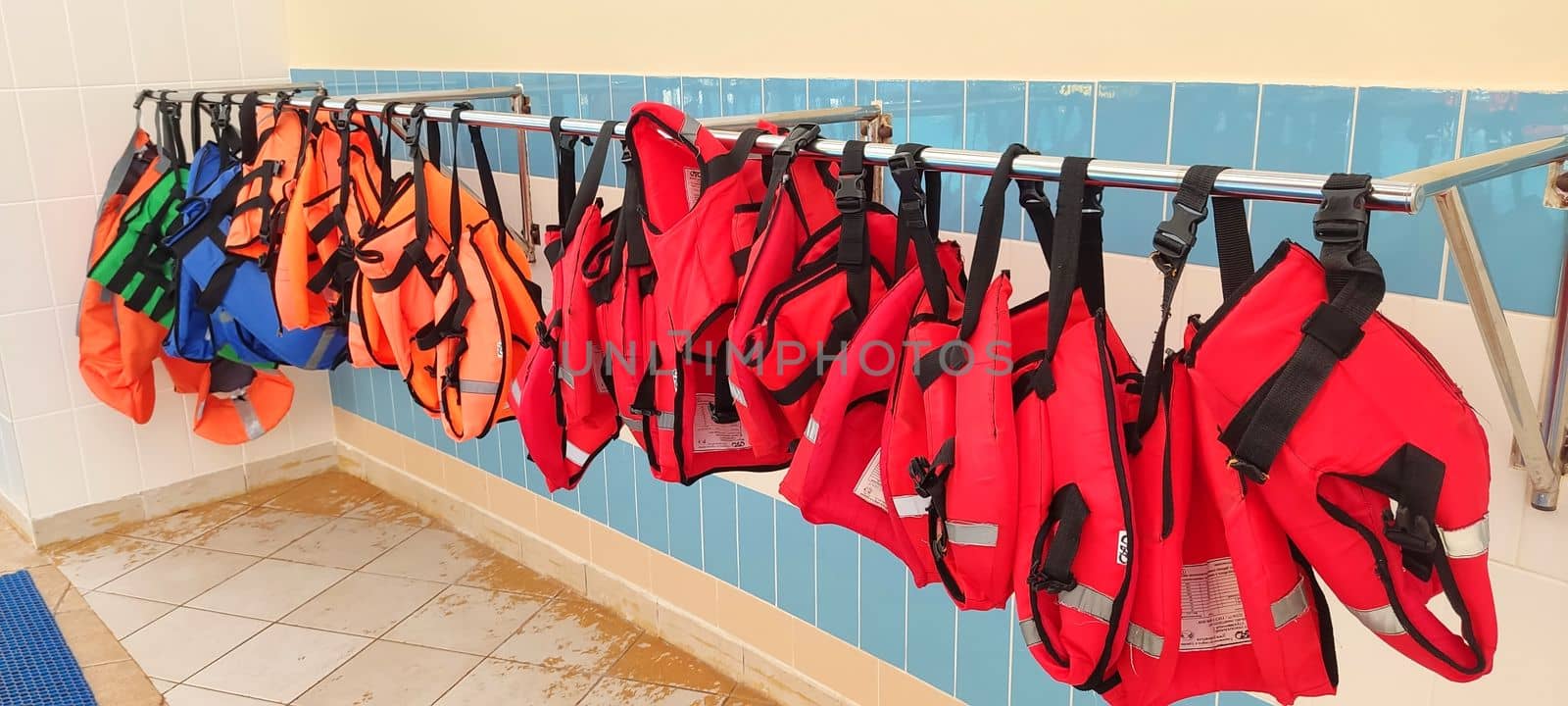 Several red and orange life jackets hang on a hanger, near the gouboi tile wall in the pool.