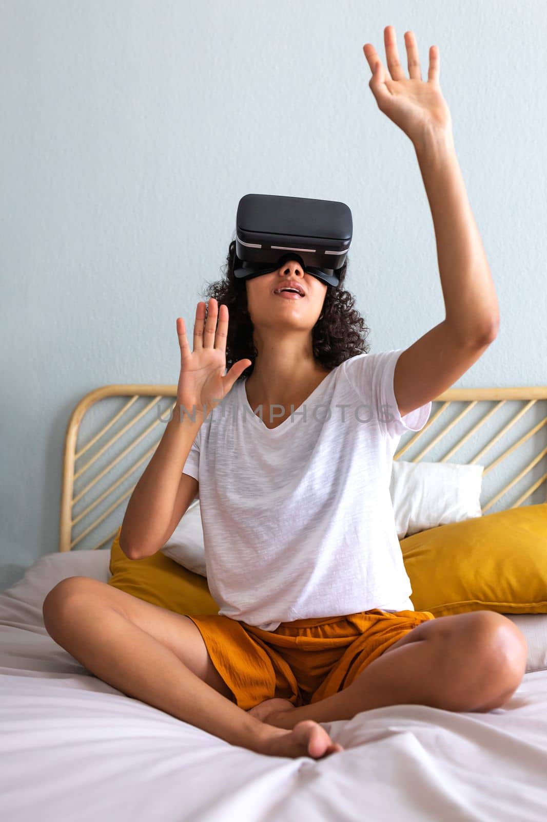 Vertical portrait of young multiracial latina woman moving hands touching objects in 3D world using VR glasses at home. Copy space. Modern technology and entertainment.