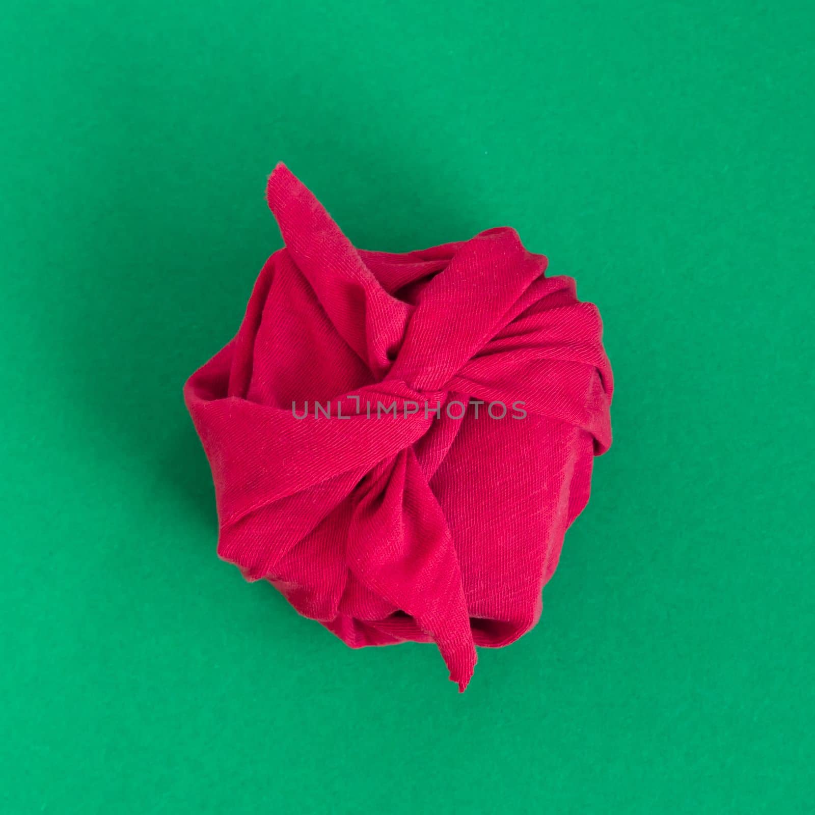 Paper free gift wrapping technique Furoshiki. Viva magenta fabric on green background. Flat lay, present box, top view. Christmas, valentines, new year concept
