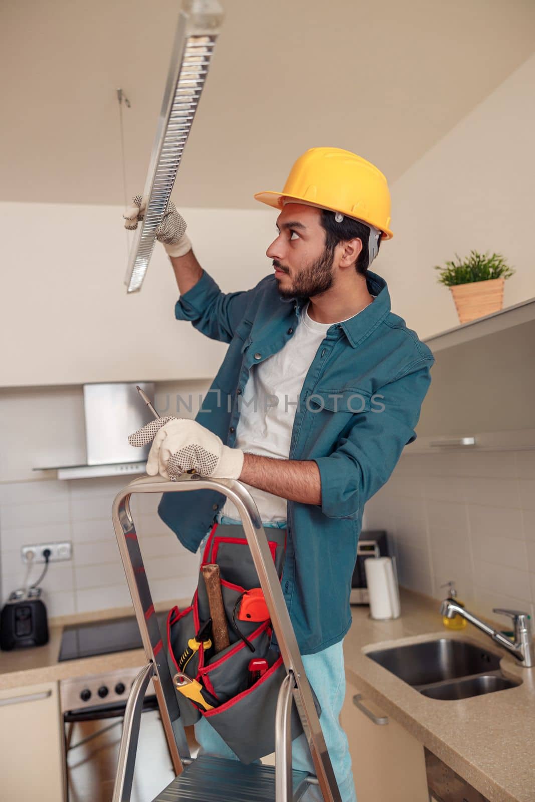 Electrician worker is installing electric lamps light in kitchen. Construction decoration concept