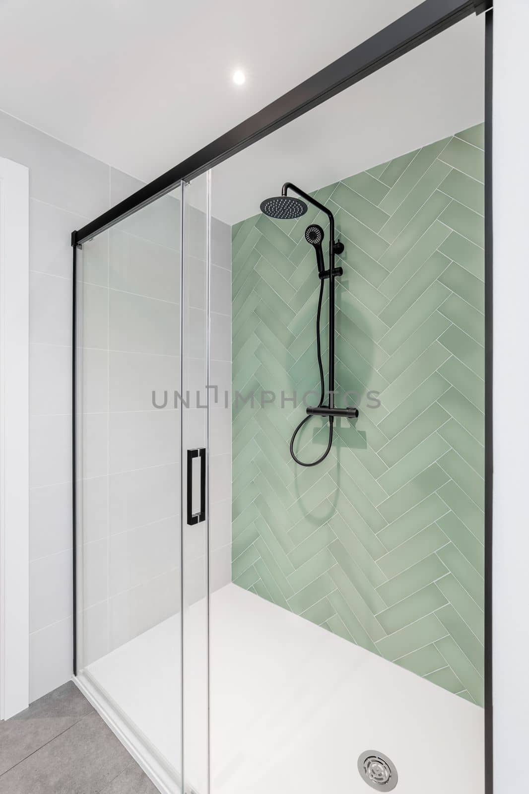 Modern bathroom with light green and white tiles, rain head, hand held shower and glass door