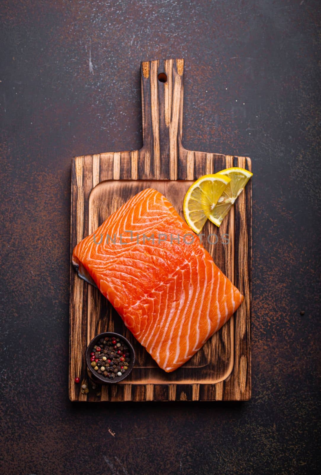 Fresh raw salmon fillet on wooden kitchen cutting board with seasonings and lemon top view on dark brown rustic background by its_al_dente