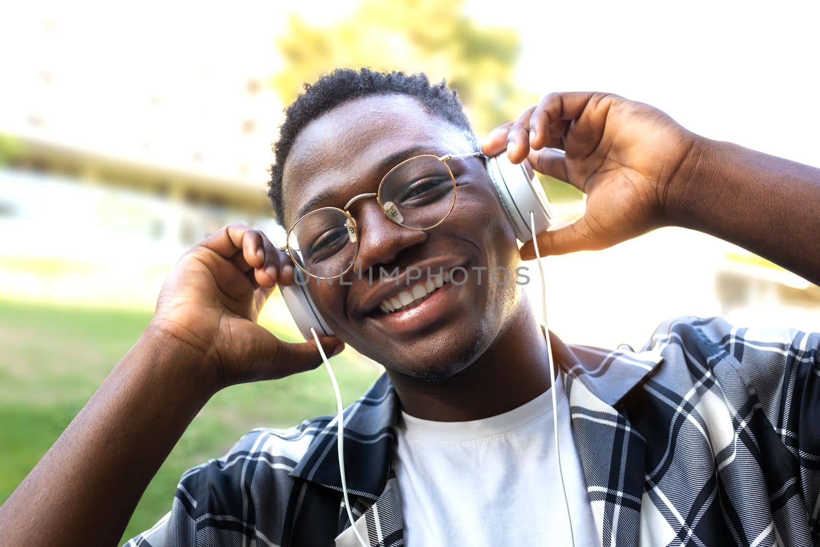 Black young man relaxing outdoors listening to music using headphones looking at camera. Lifestyle concept.