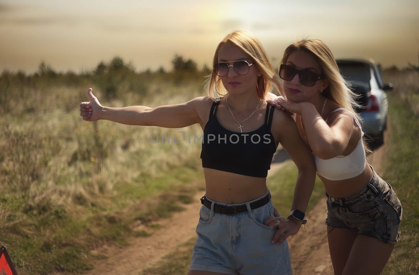 an accident on the road, a car broke down, two beautiful girl models are hitchhiking a car. Showing the thumb up. Problem with the car. Friends waiting for service. In the countryside . by marselin888