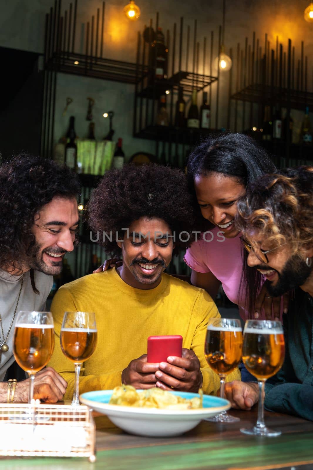 Group of multiracial happy friends looking at phone in a pub having drinks. Vertical image. Having fun.