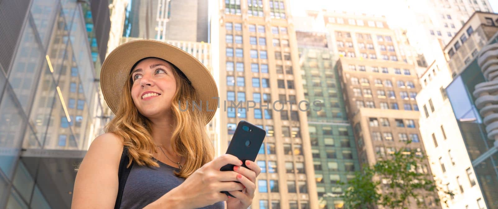 Attractive positive female holding mobile phone in hand looking at modern city. High quality photo