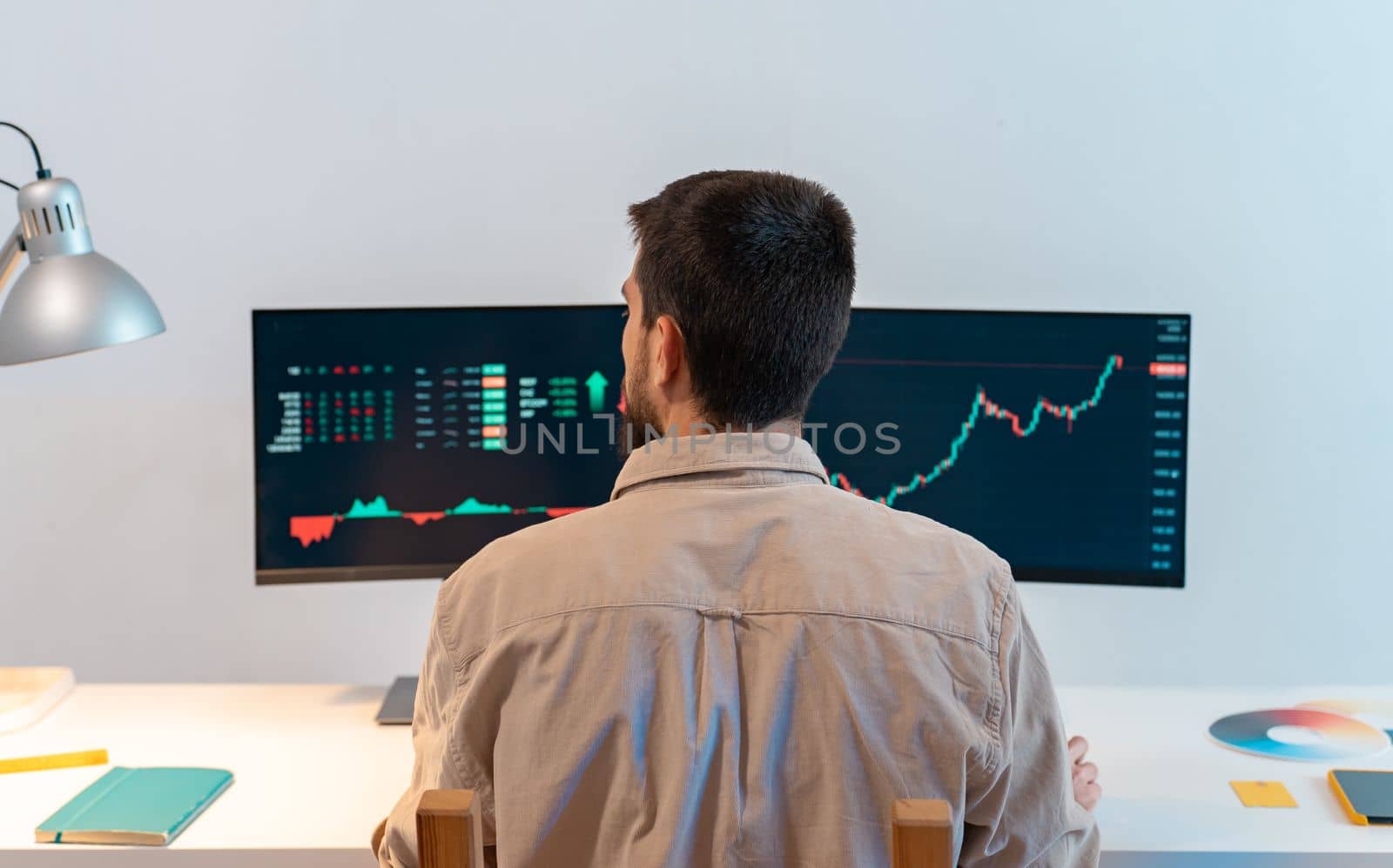 Rear view of young caucasian man finance broker analyzing stock graphs while trading from home. High quality photo
