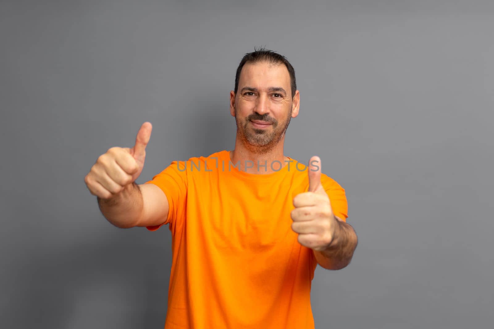 Attractive cheerful hispanic man with a beard wearing t-shirt standing isolated over gray background, showing thumbs up