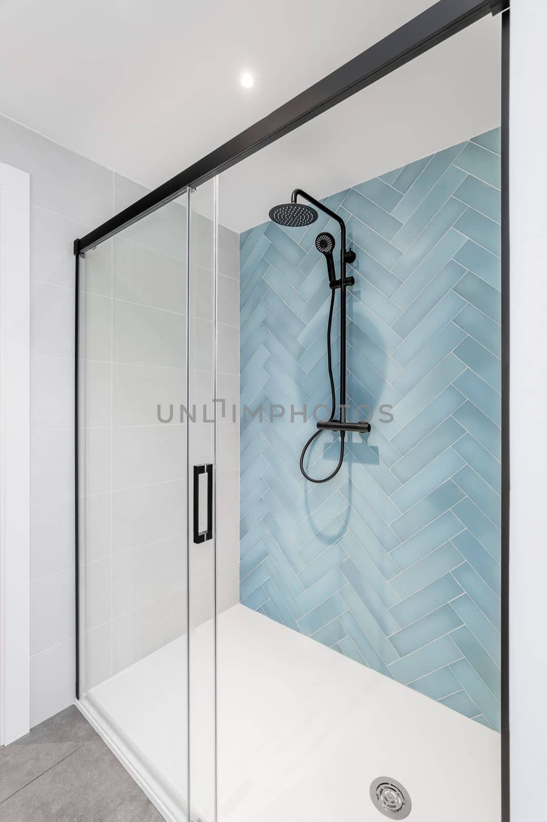 White bathroom with glass shower, walls are decorated with herringbone tiles in pale blue Black shower system enclosure with dark matte framed sliding glass door. Bright modern and stylish bathroom