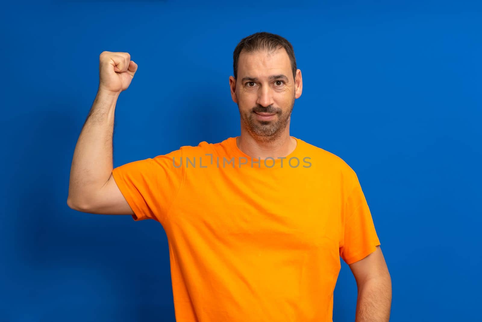 Excited joyful man in orange t-shirt standing isolated over blue background, celebrating success