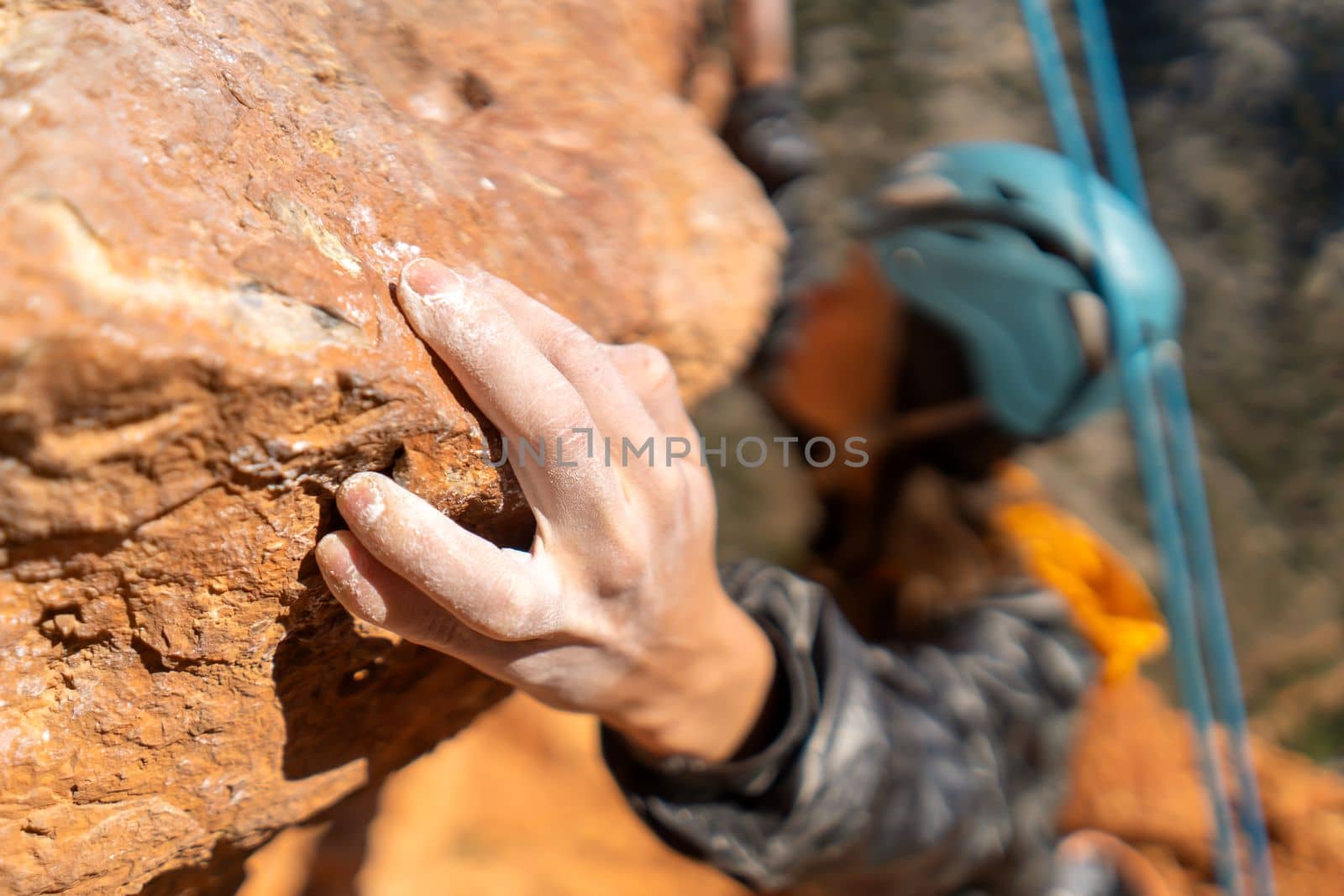 Young girl is engaged in extreme sports, fearlessly climbs up the rock using white magnesia powder, holds her hand to the ledge in the relief, close-up view, focus on the finger, the girl is blurred.